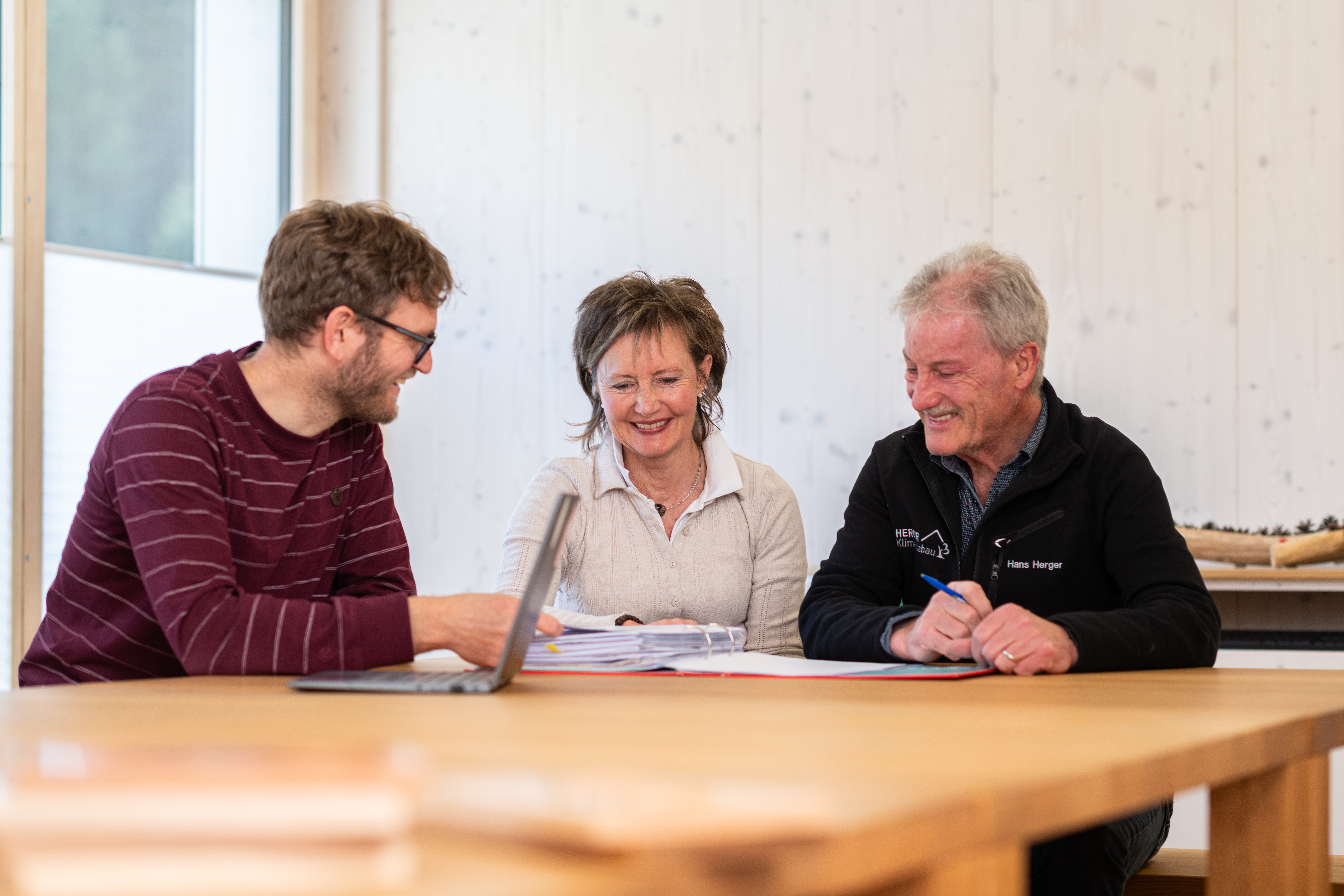 Un conseiller en assurances de la Mobilière mène un entretien de conseil avec deux clients. Toutes les personnes discutent autour d’une table en bois.
