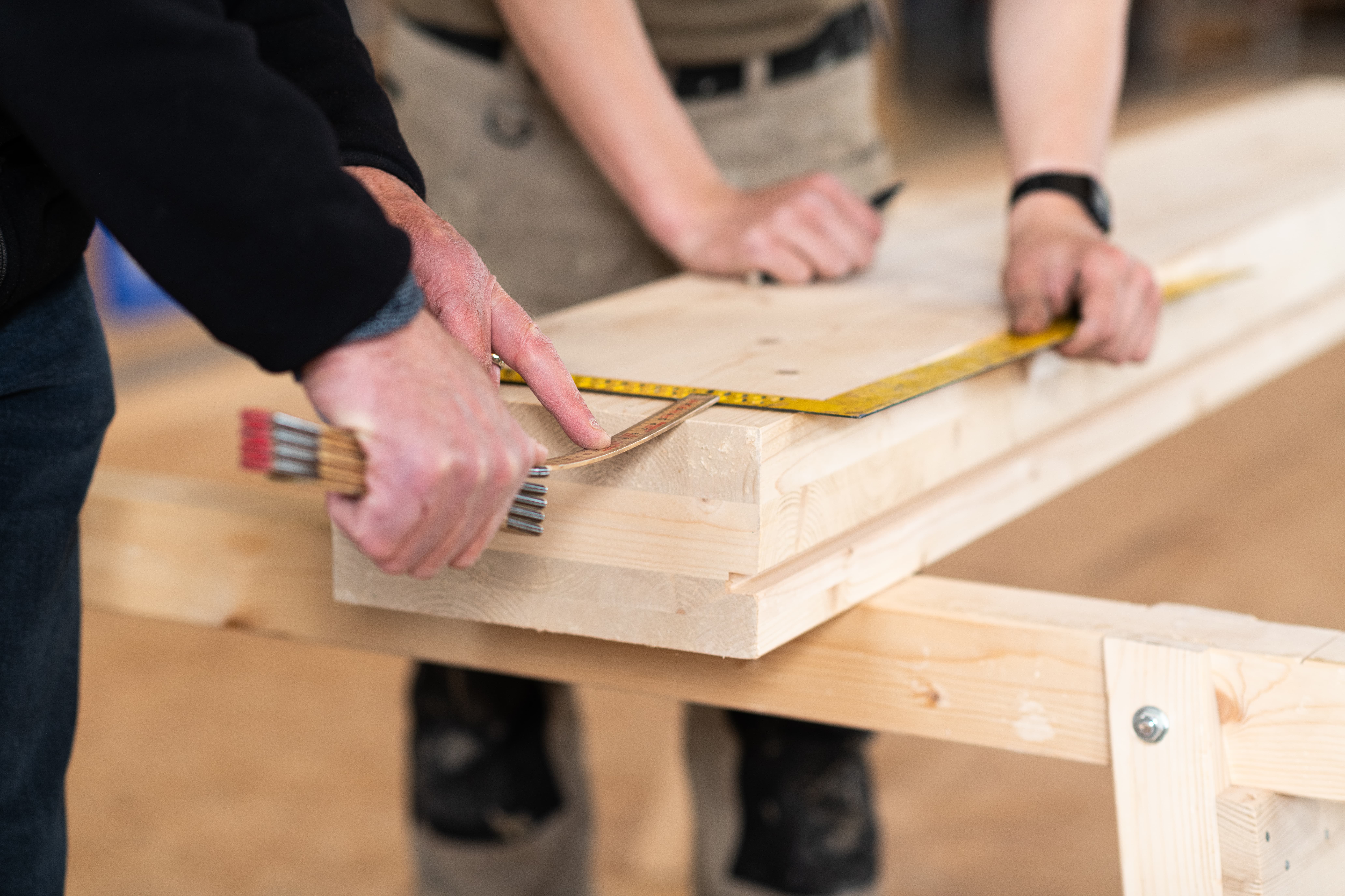 Deux personnes prennent les dimensions d’une poutre en bois.