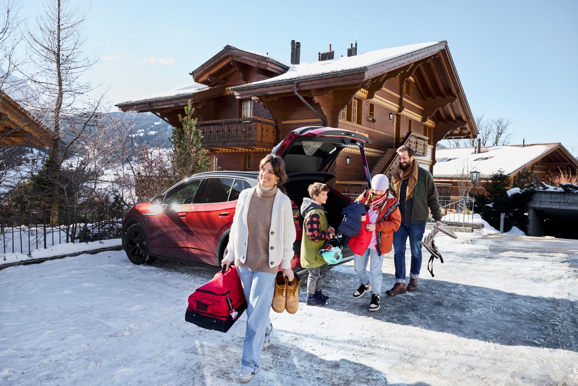 Familie mit Kindern packt Gepäck aus dem Kofferraum eines Autos vor einem Chalet im Schnee. Symbolbild für Schneeräumung in der Schweiz.