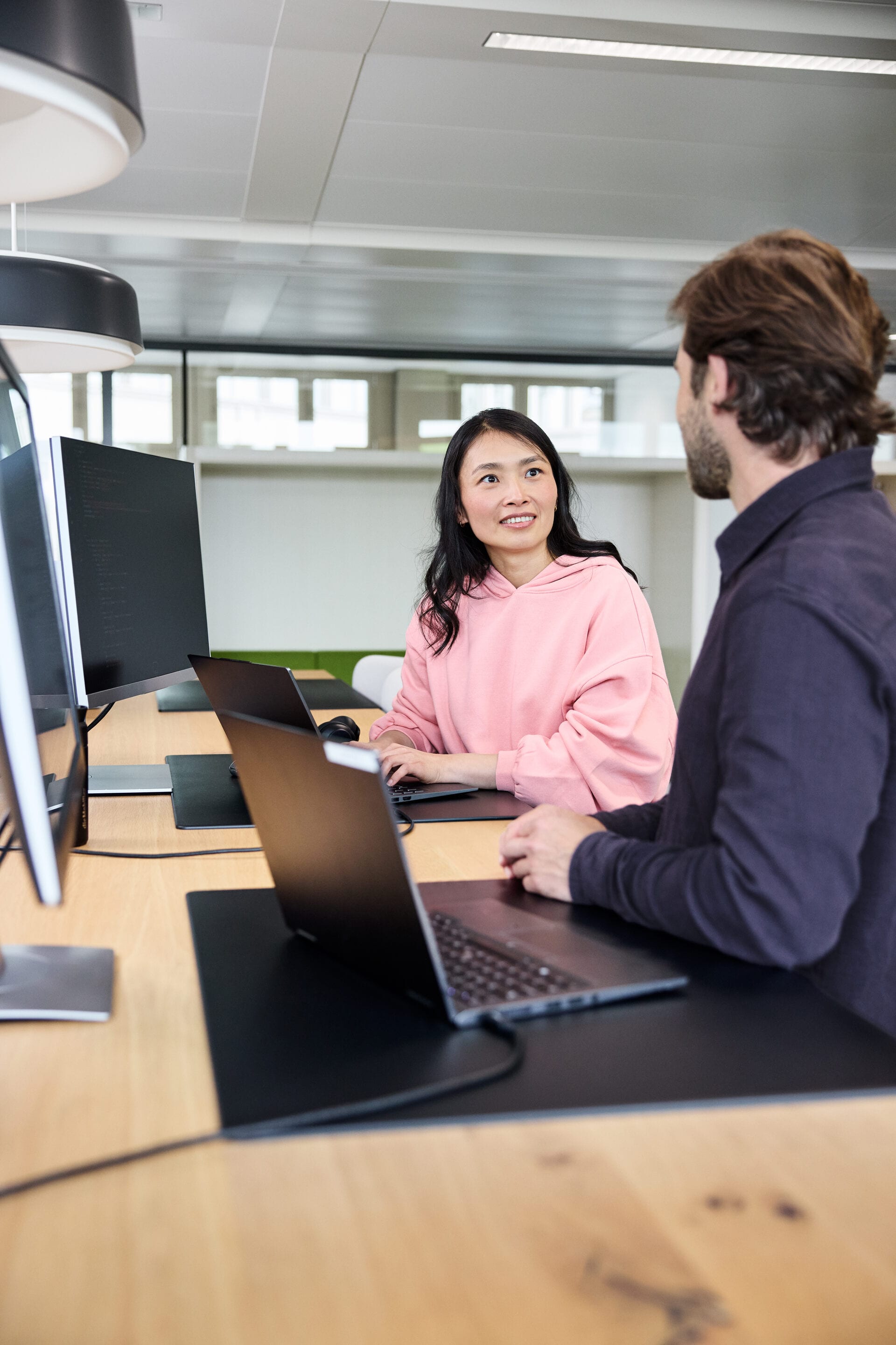 Zwei Mitarbeitende sitzen an den Laptops und unterhalten sich