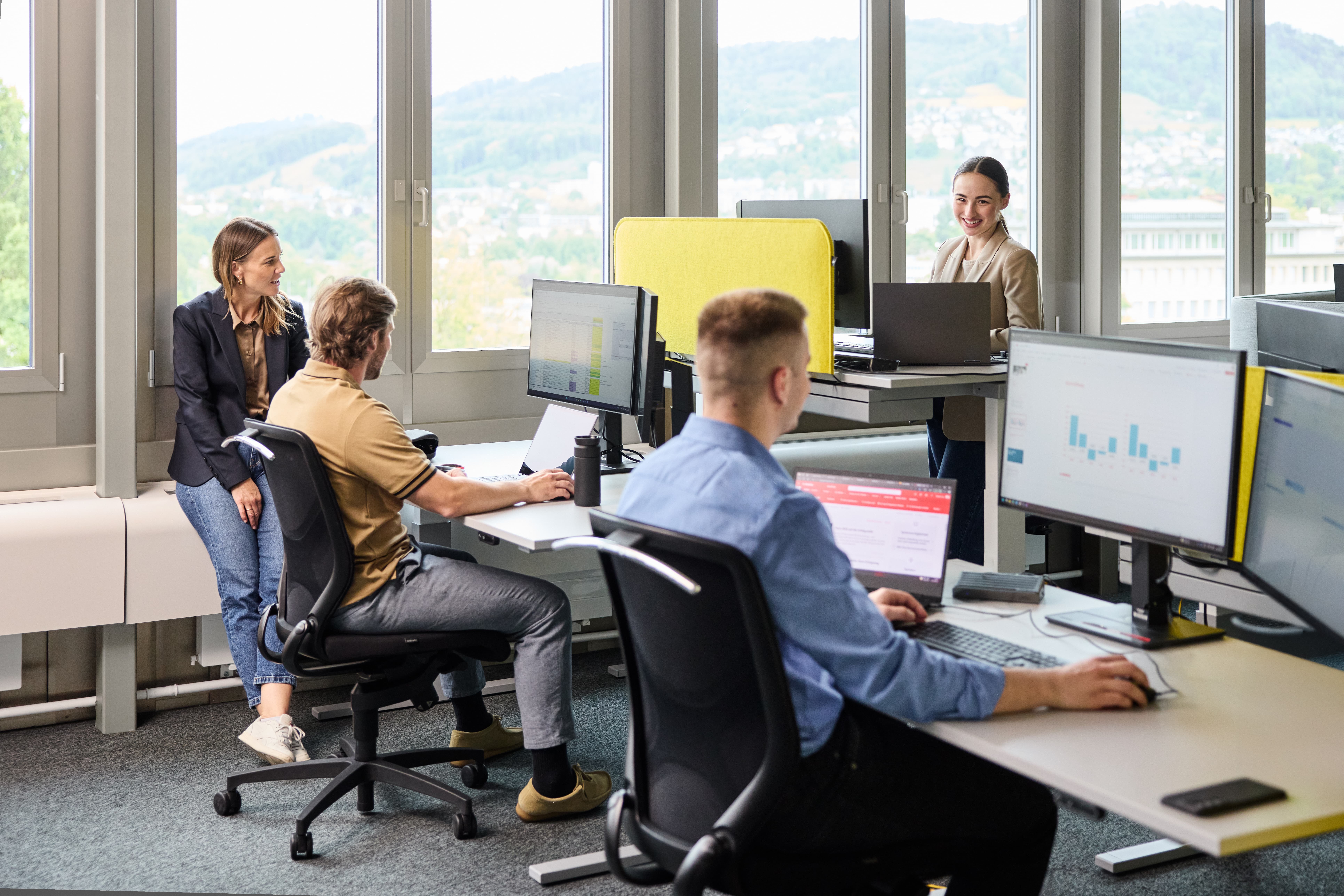 Mitarbeitende im Gespräch und am Arbeiten im Büro vor Bildschirmen