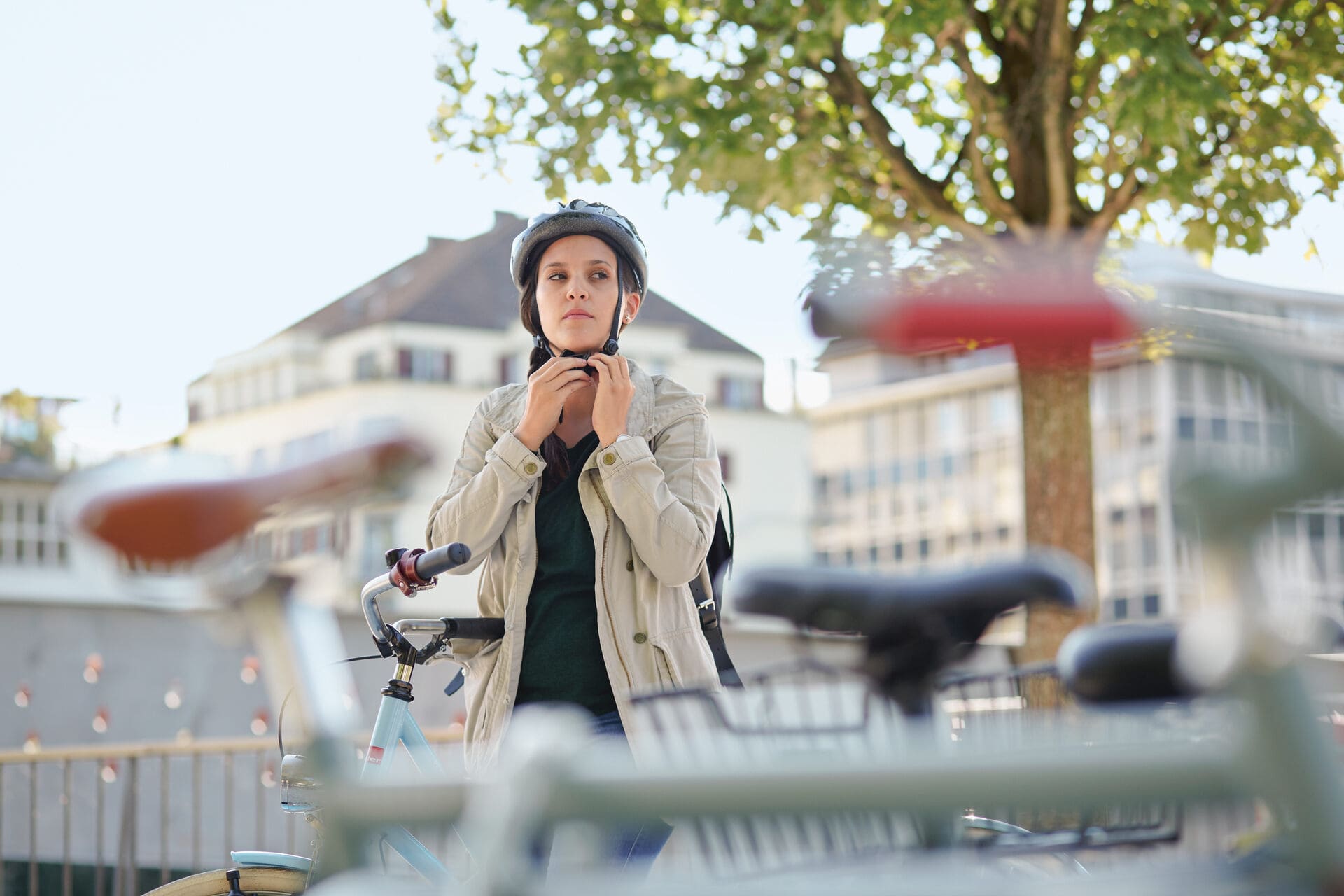 Junge Frau steht bei einem Fahrradständer und zieht ihren Helm an.