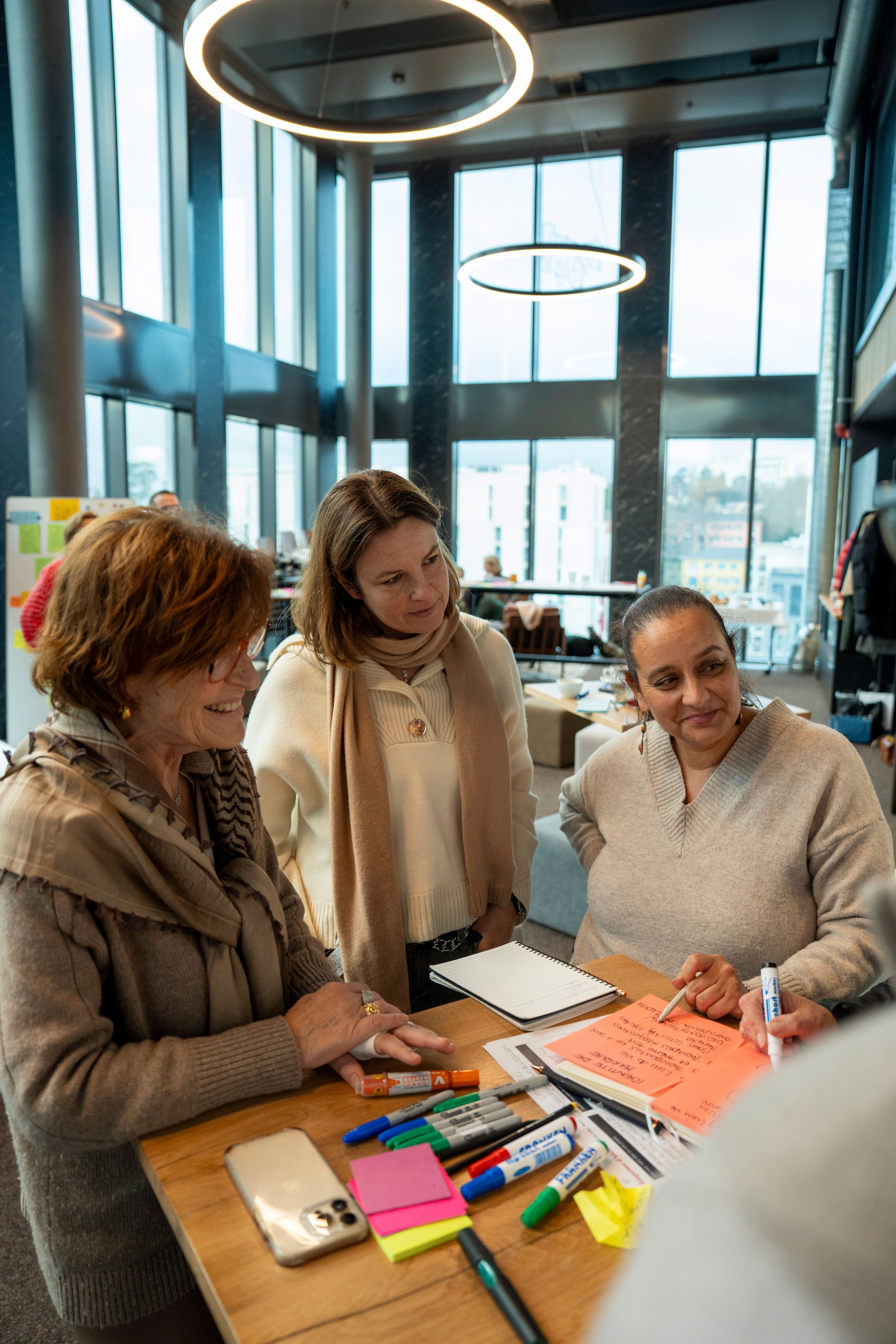Trois participantes d’un atelier se tiennent autour d’une table haute.