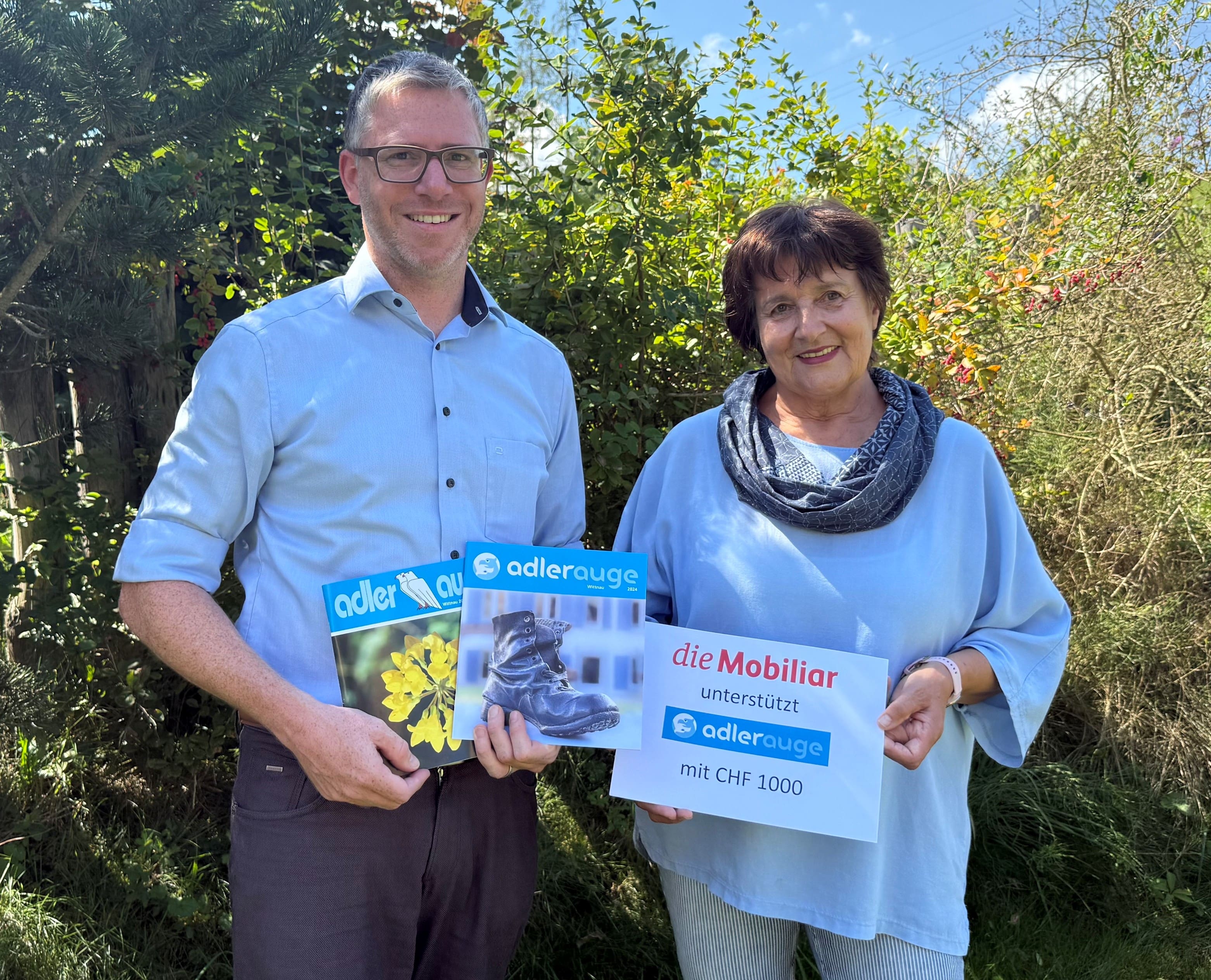 2 Personen halten einen Mobiliar-Check und 2 Adlerauge Magazine.