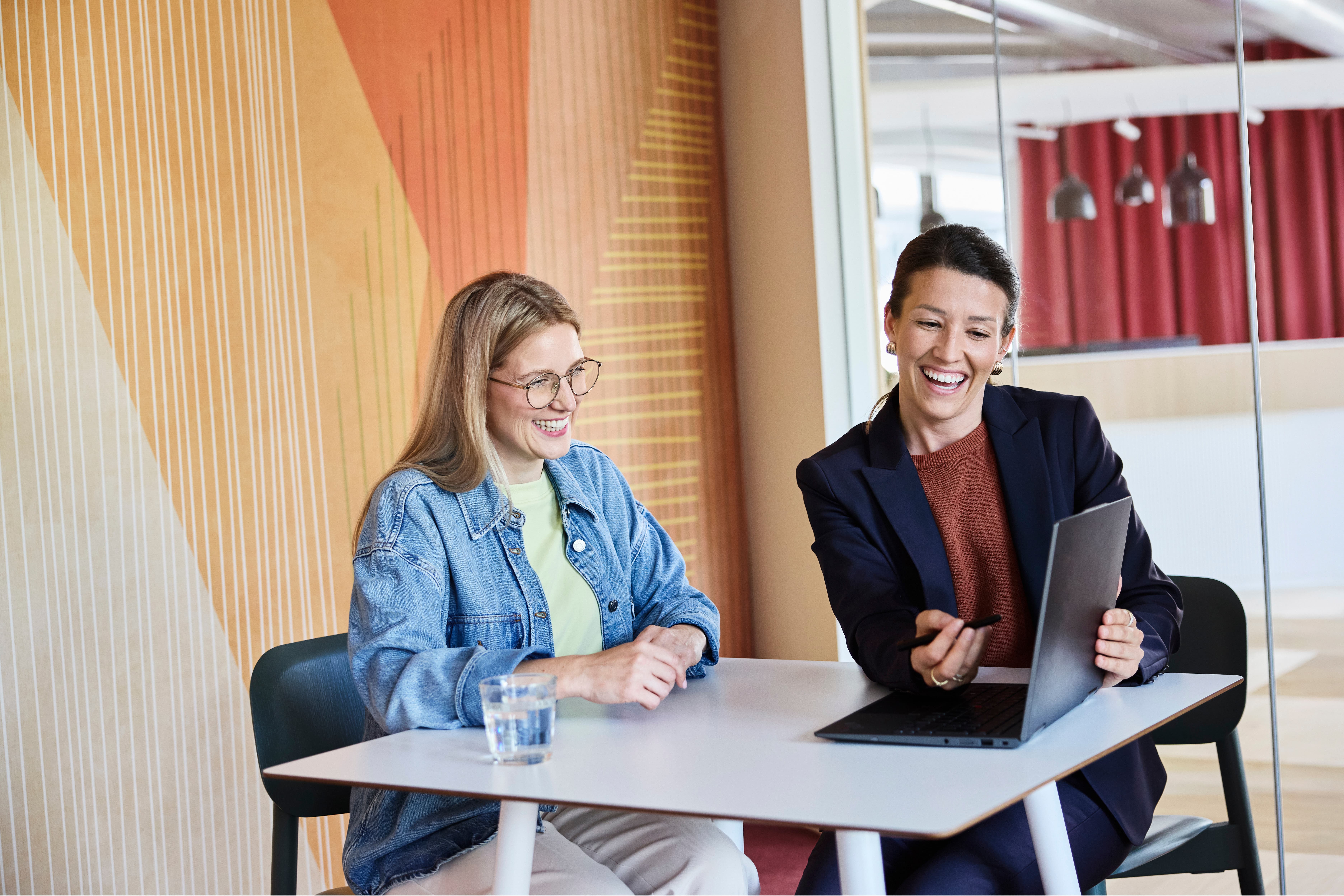 Due donne sedute vis-à-vis, guardano lo schermo di un computer portatile e discutono di qualcosa