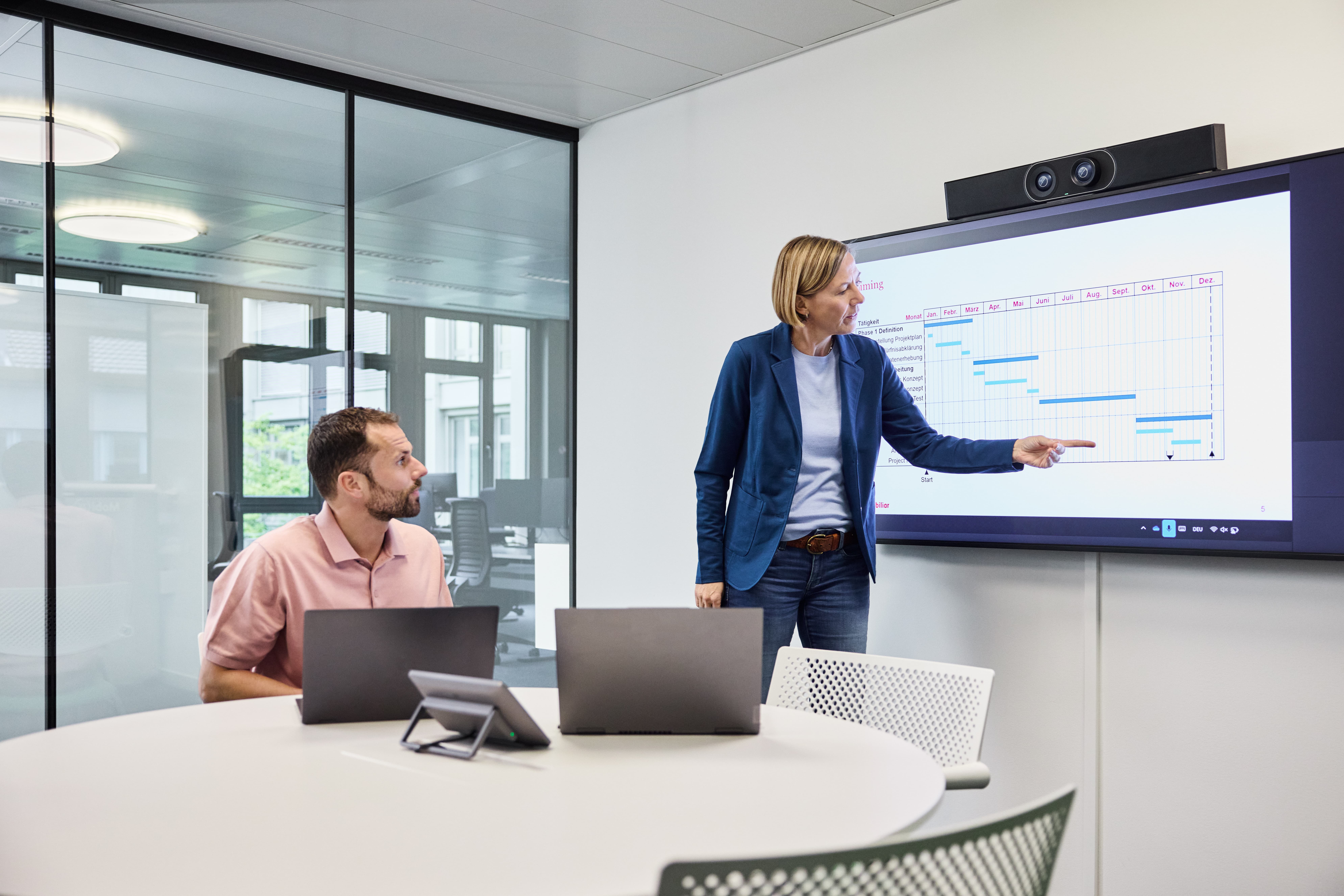 Mann steht vor Wand mit vielen Bildschirmen und spricht