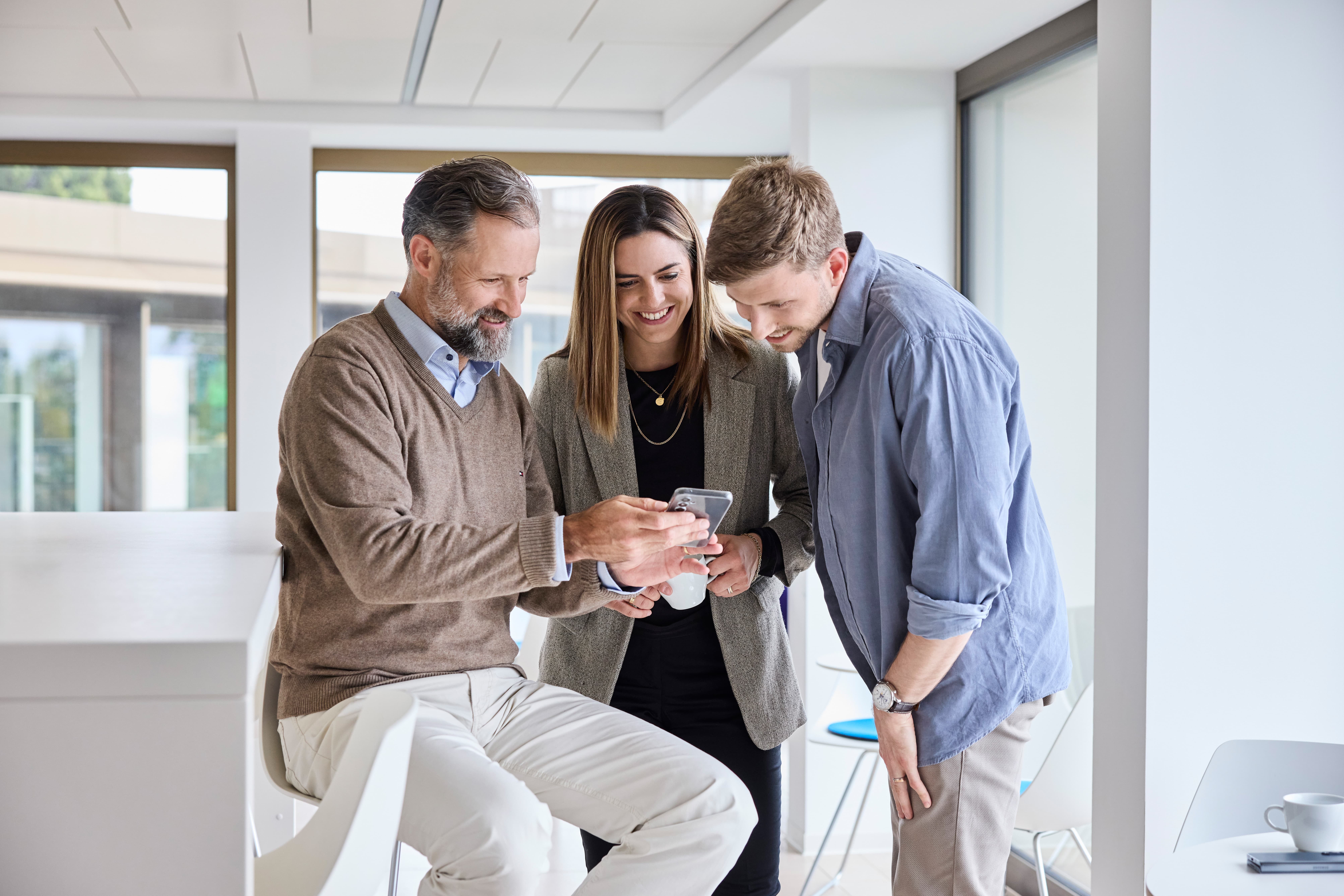 Mitarbeitende schauen in einer Pause zusammen auf ein Handy.
