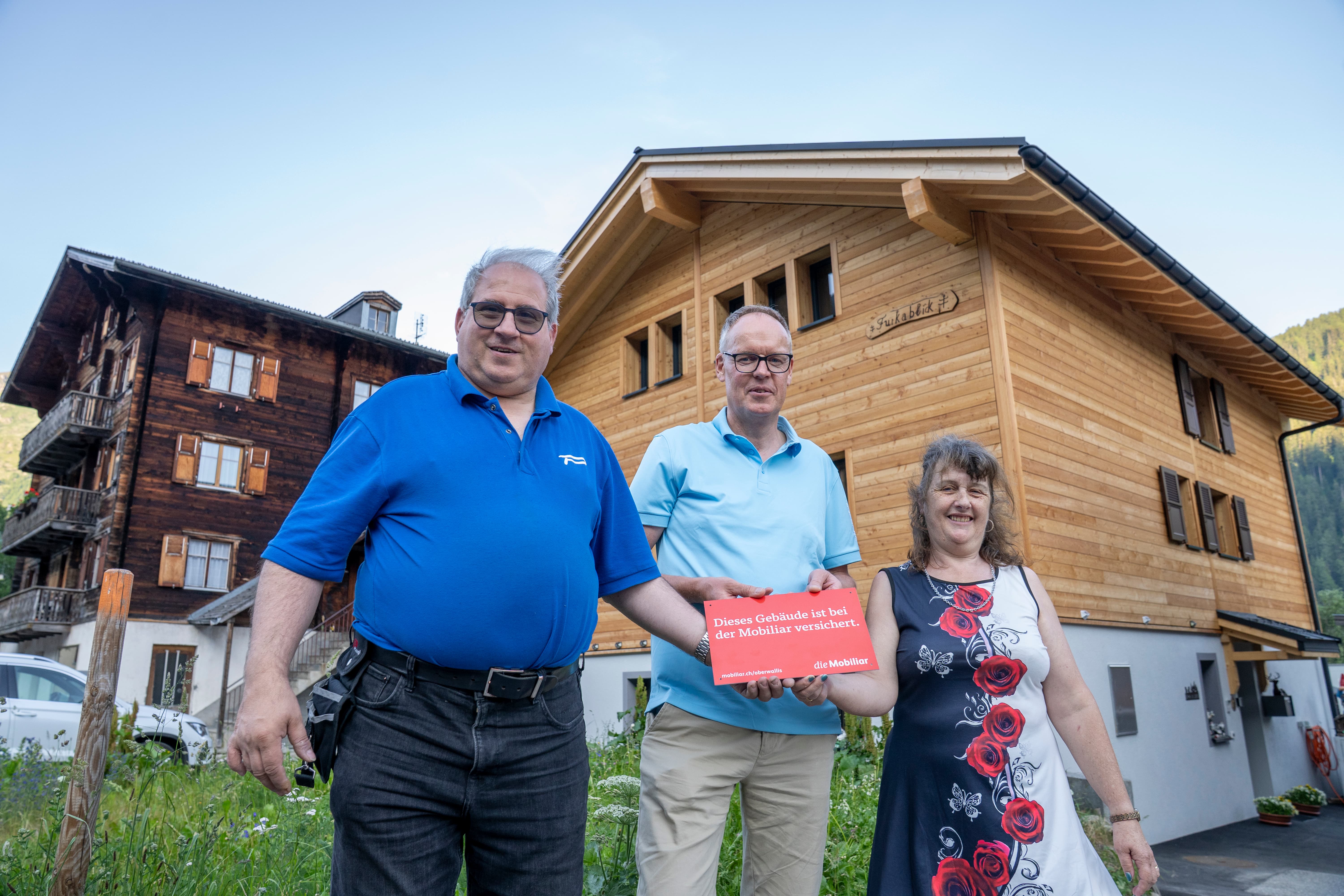 Trois personnes devant une nouvelle maison en bois.