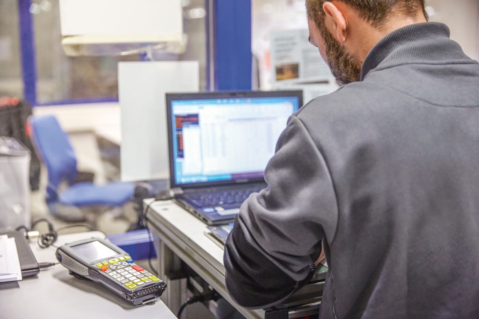 Blick von hinten auf einen Mann, der am Schreibtisch sitzt, vor ihm ein offener Laptop. Symbolbild zum Thema Zahlungsverzug Kunden.