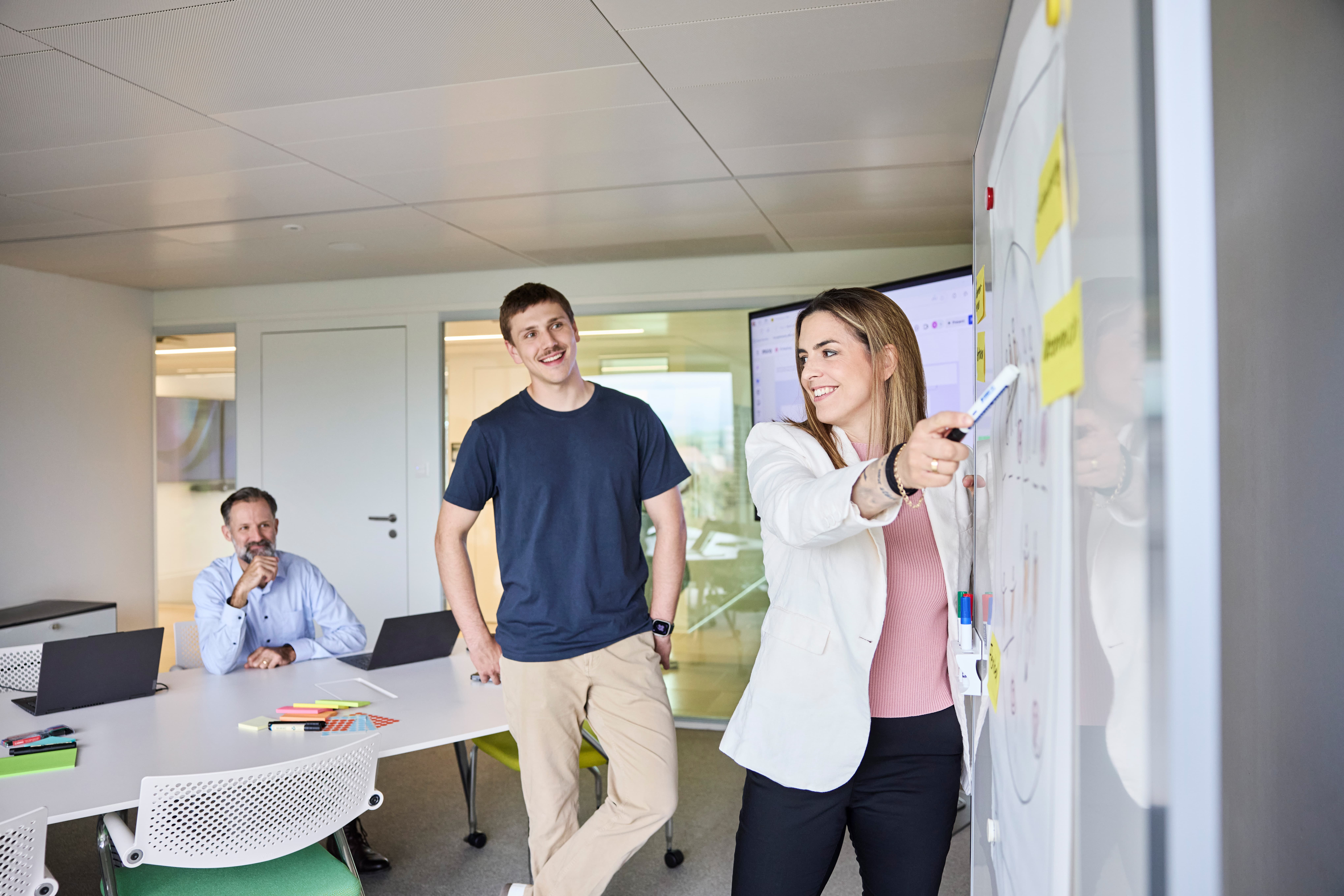 Mitarbeiterin zeigt ihren Kollegen etwas am Whiteboard 