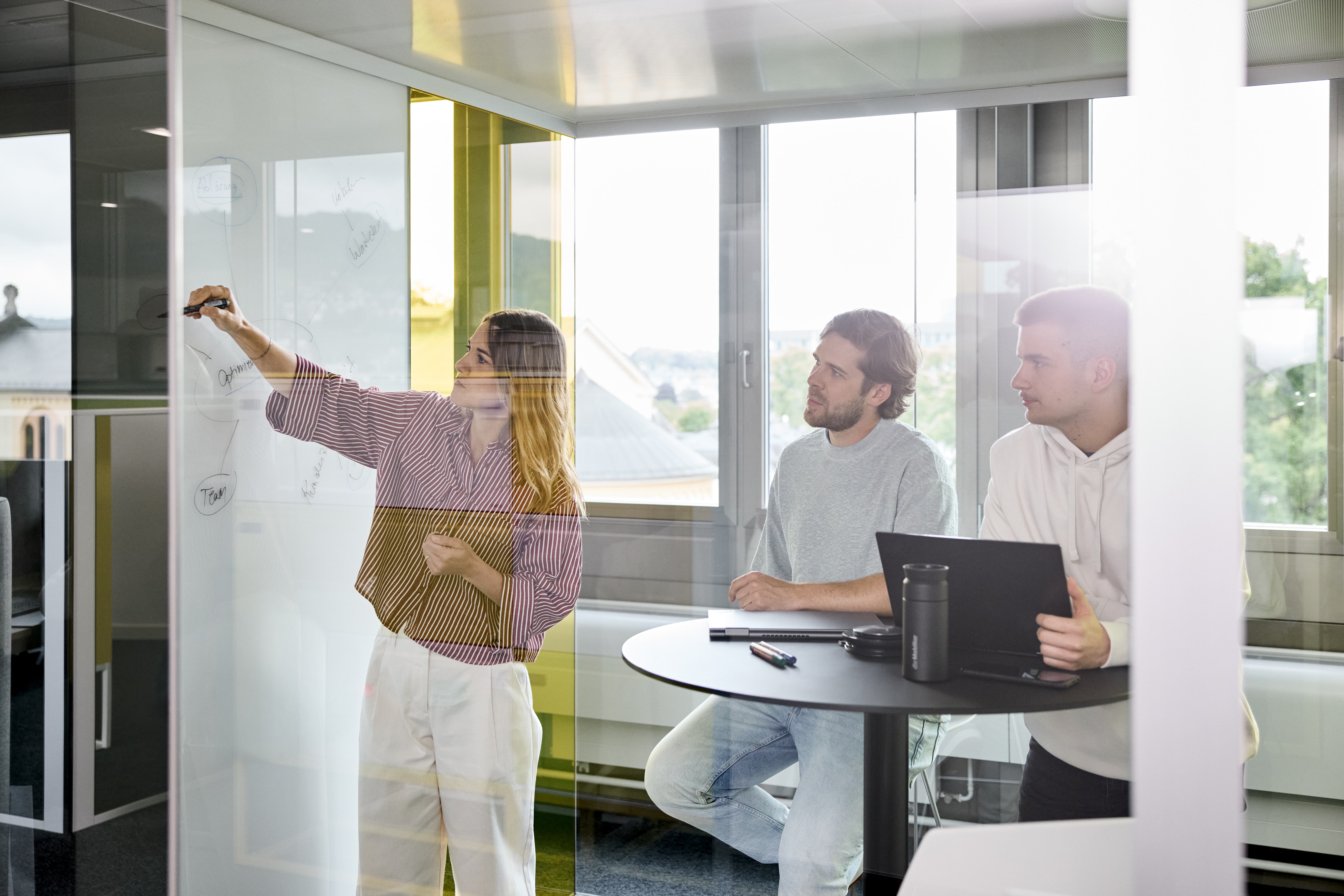 Mitarbeiterin erklärt ihren Kollegen etwas anhand einer Skizze