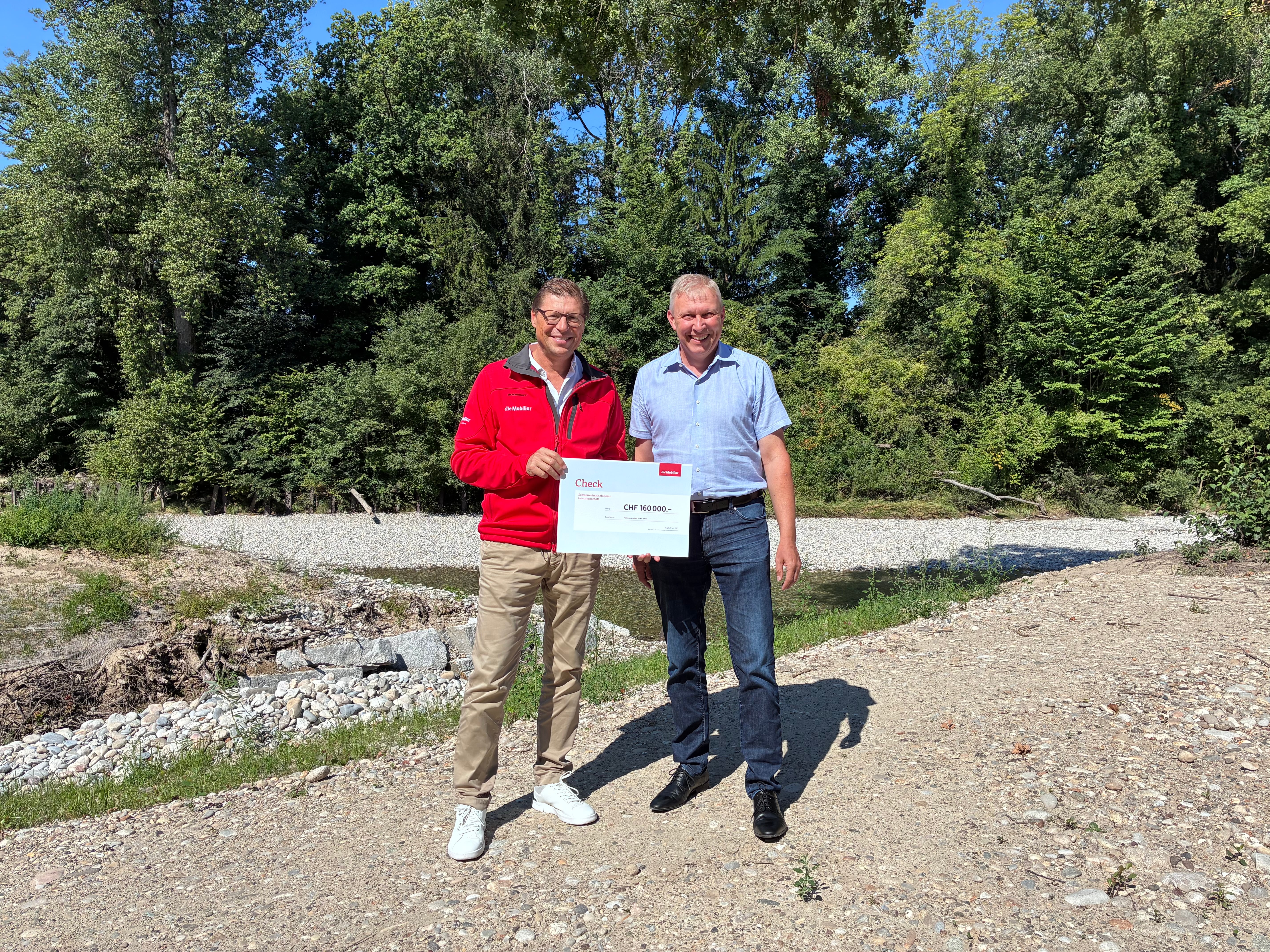 Zwei Männer stehen mit einem Check vor einem Präventionsprojekt.
