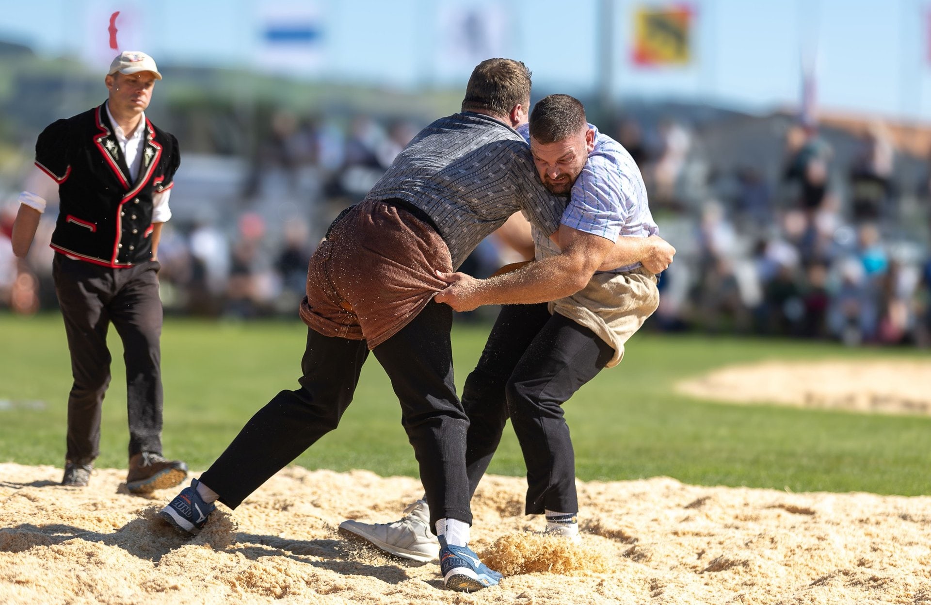 Benjamin Gapany en plein combat de lutte suisse, concentré et en prise avec son adversaire sous les yeux du juge.