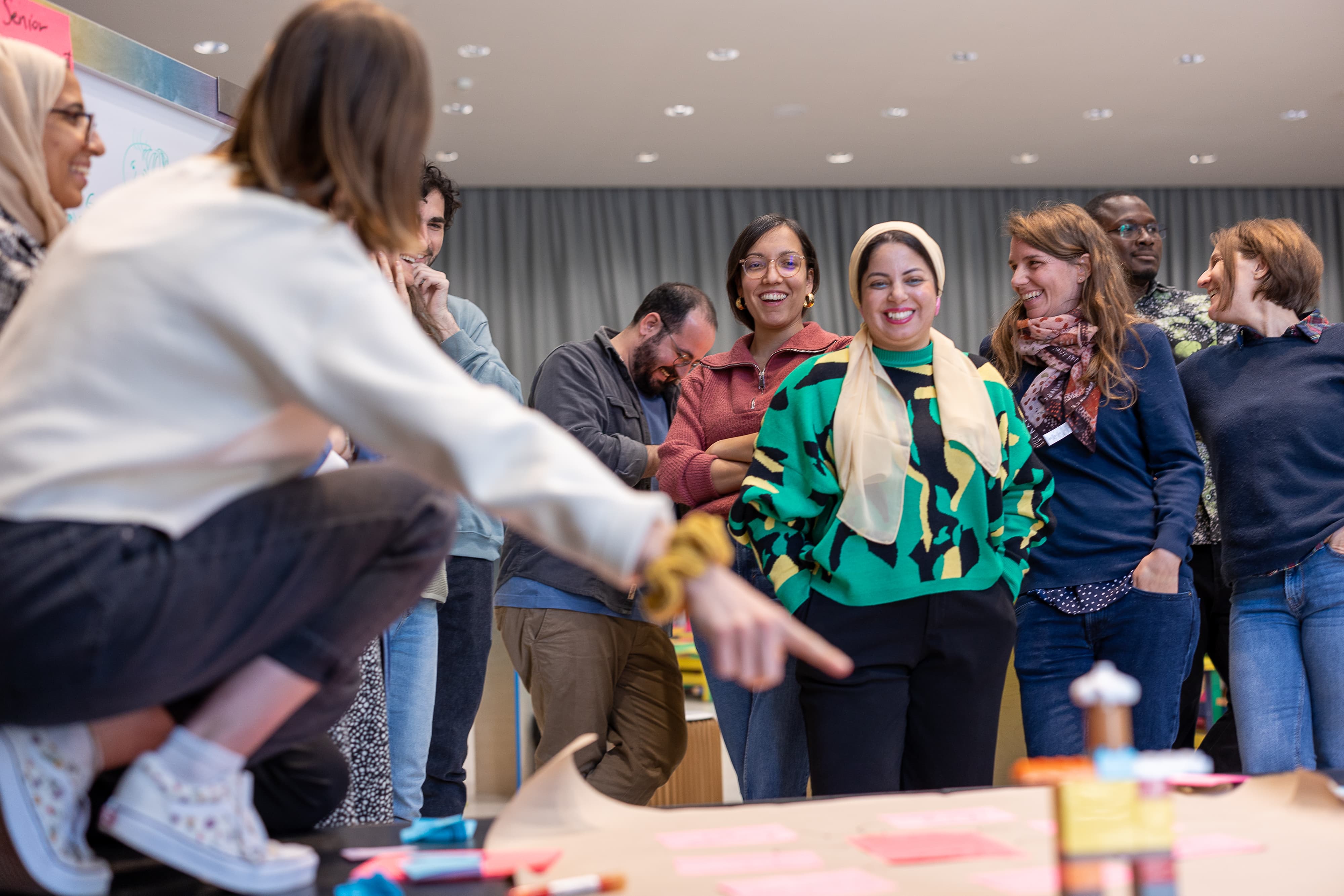 Eine dynamische Gruppe diskutiert die Ergebnisse aus dem Mobiliar Forum Workshop, eine Person zeigt eine Figur, der Rest der Gruppe schmunzelt oder nickt zustimmend.