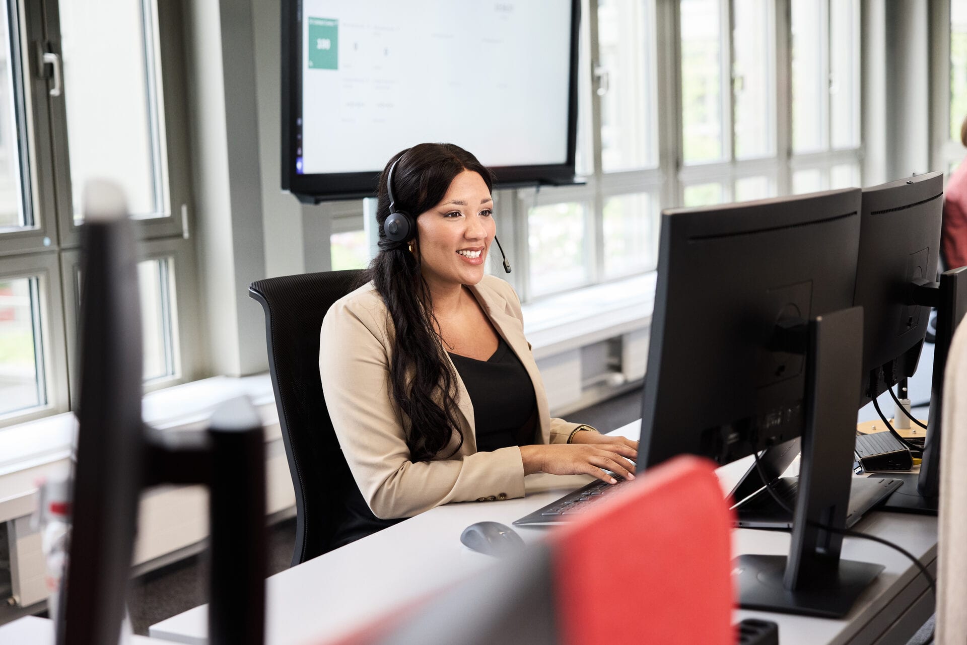 Frau steht am Arbeitsplatz mit Headset und telefoniert