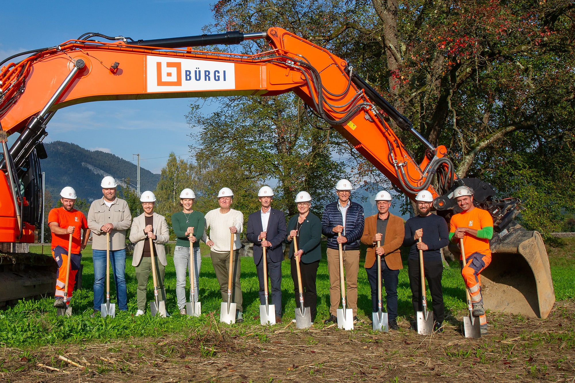 11 Leute stehen vor einem Bagger.