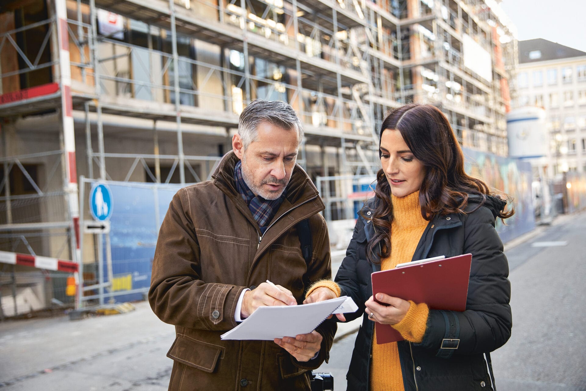 Ein Mann und eine Frau stehen vor einem Haus und schauen sich Dokumente an