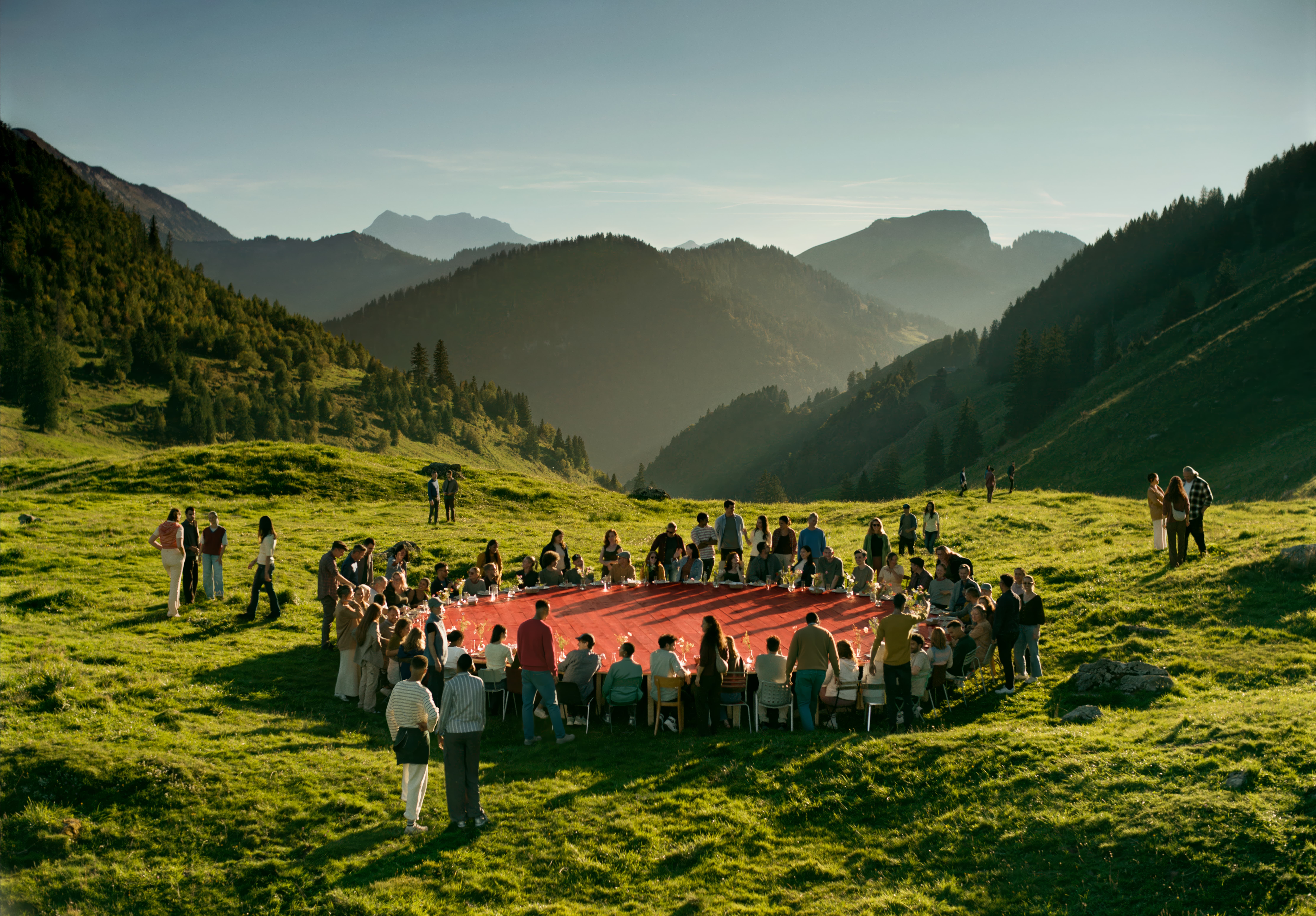 Eine Gruppe von Leuten sitzen an einem grossen roten runden Tisch auf einer grünen Wiese