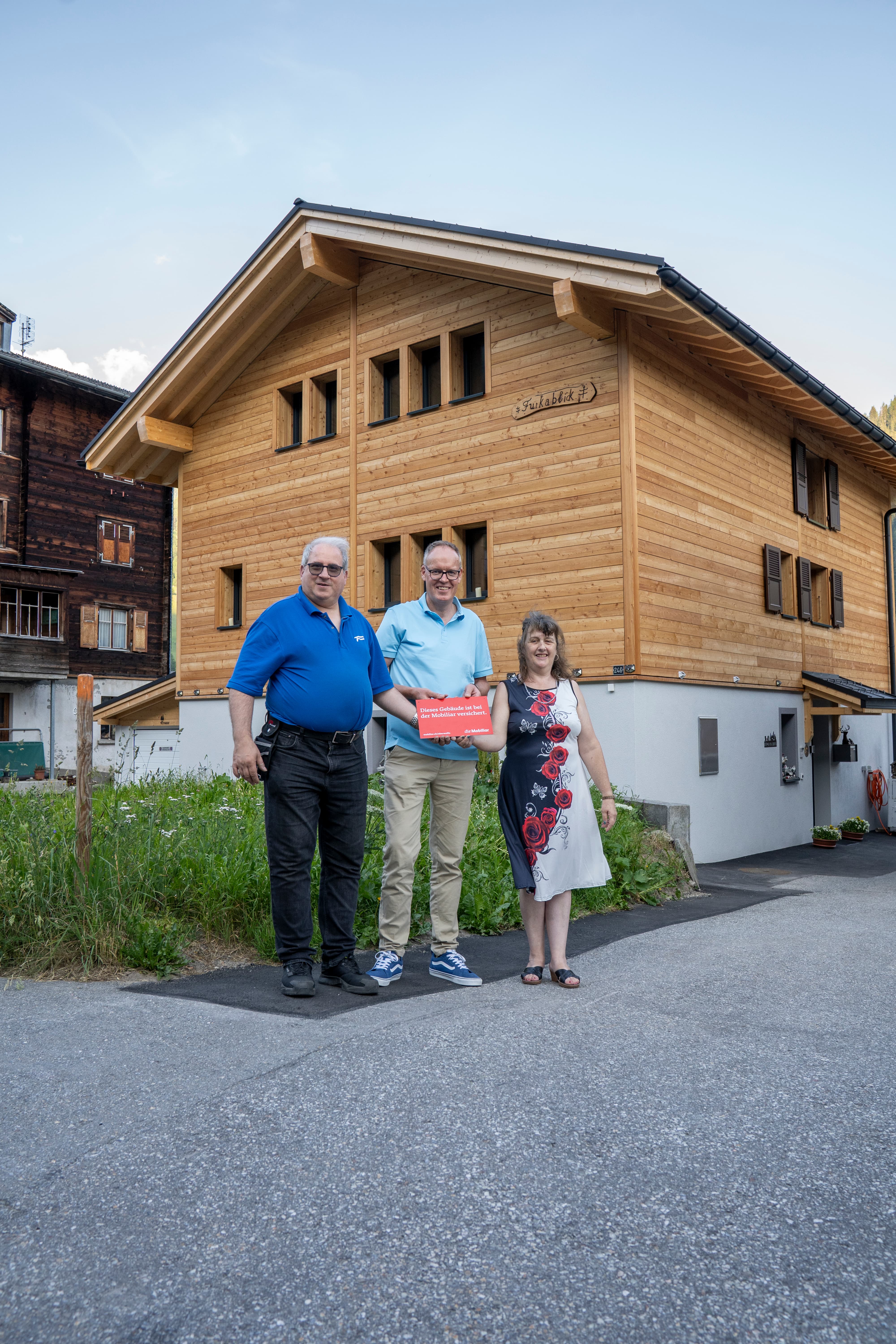 Vor einem Holzhausneubau stehen drei Personen.