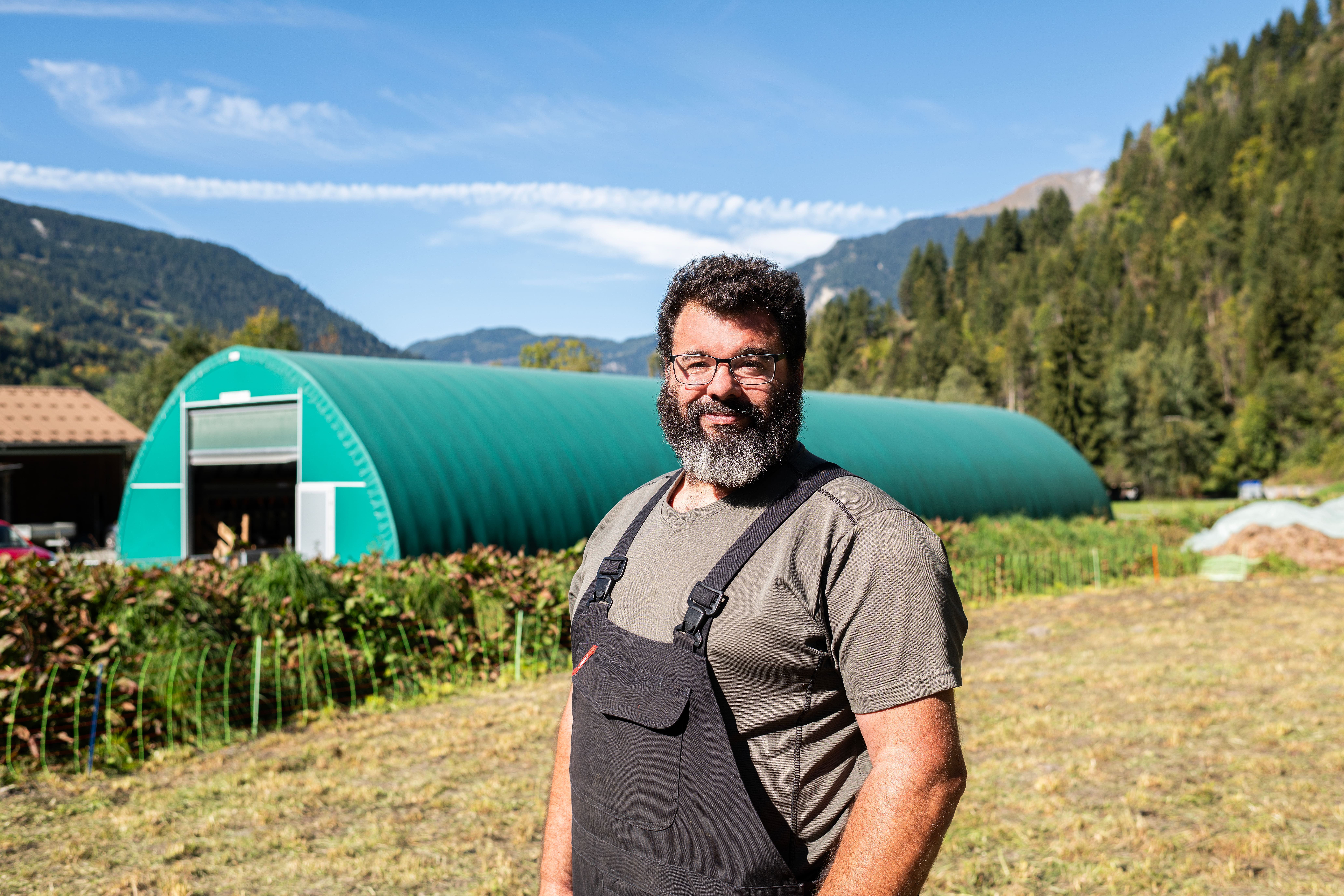 Lucien Fellay se tient devant son étable provisoire, un tunnel agricole recouvert de bâches vertes.
