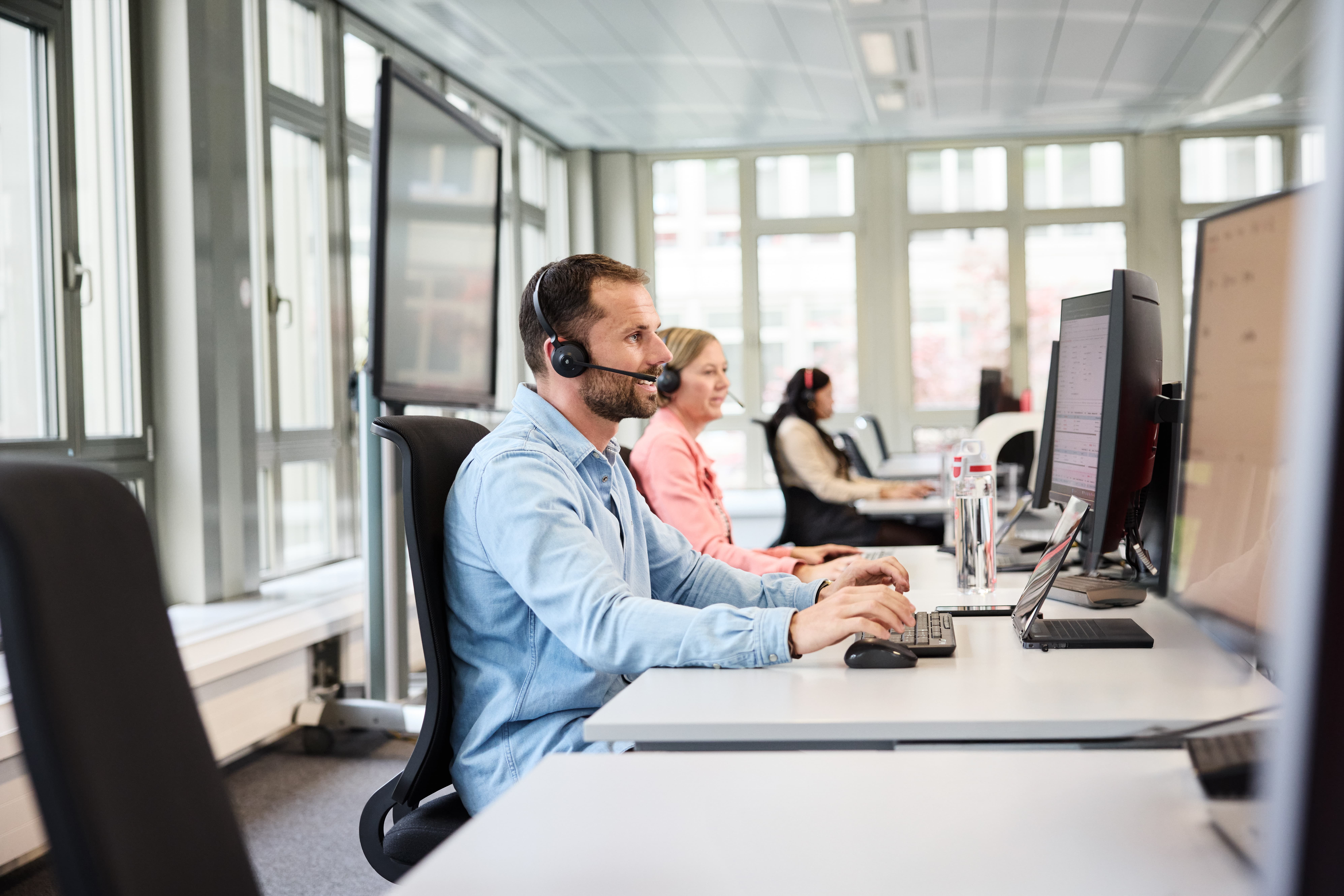 Mitarbeiter mit Headset während eines Calls am Computer arbeitend 