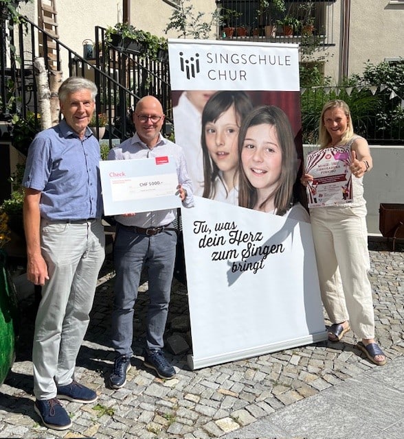 Urs Haslebacher (links), Präsident der Singschule Chur, und deren musikalische Leiterin Liliane Köhli nehmen den Check von Versicherungs- und Vorsorgeberater Stefan Walter entgegen.