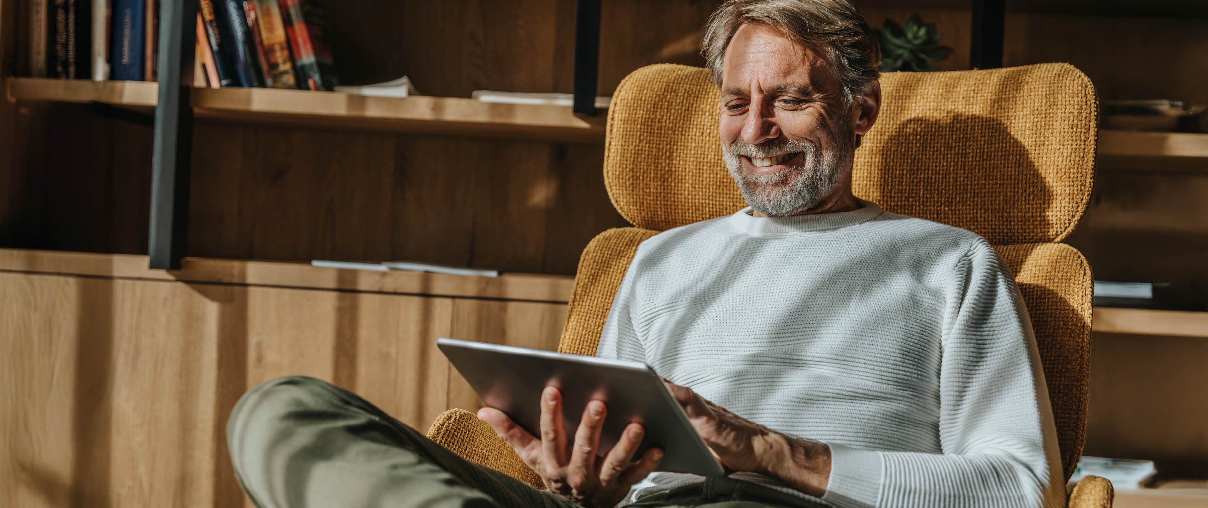 ein ältere Mann sitzt mit dem iPad in einem Sessel