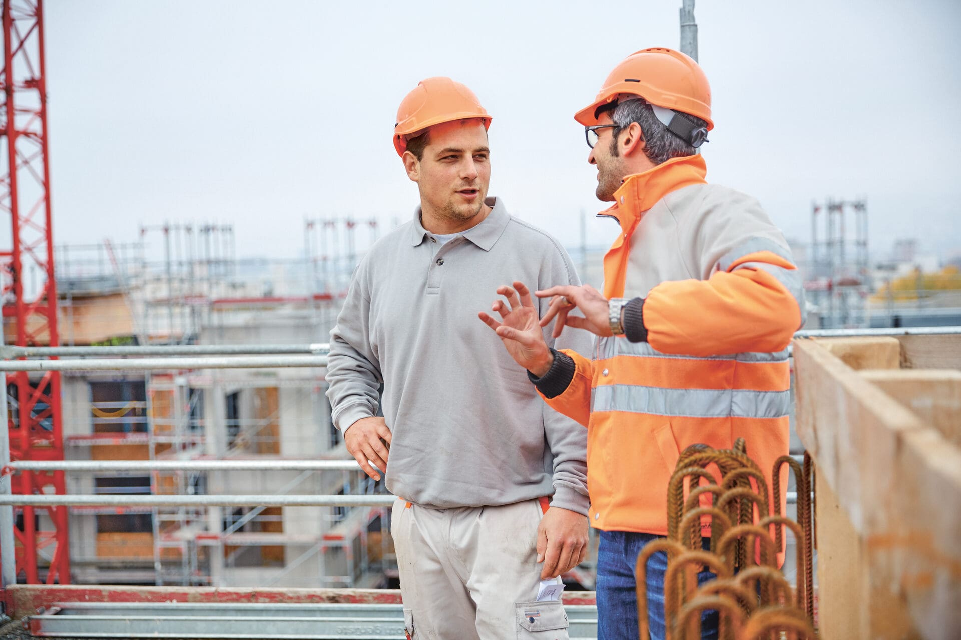 Zwei Männer stehen auf einem Gerüst einer Baustelle mit Bauhüten und besprechen die Bauplanung.