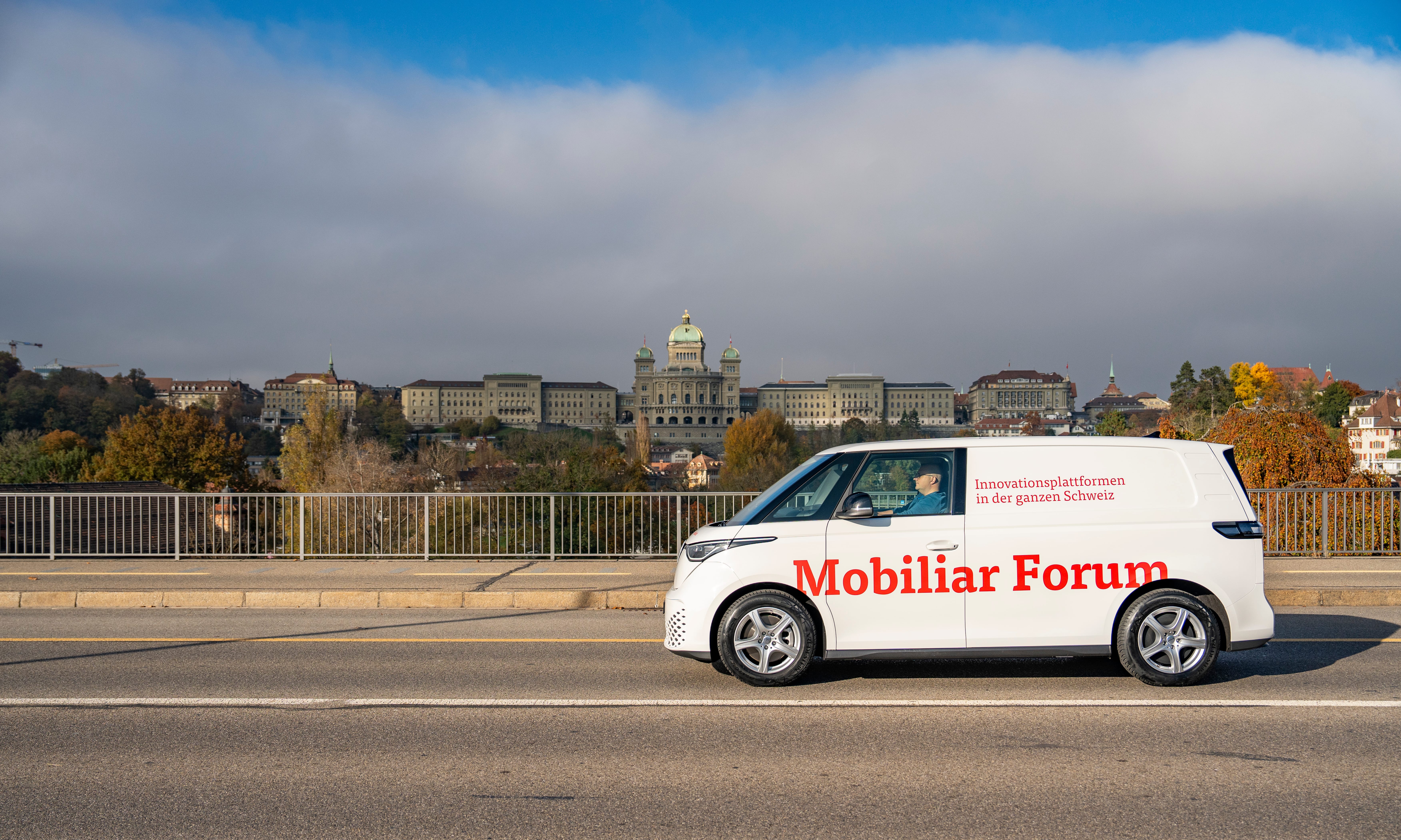 Une camionnette blanche portant l’inscription Mobiliar Forum traverse le Monbijoubrücke. À l’arrière-plan, on aperçoit le Palais fédéral.