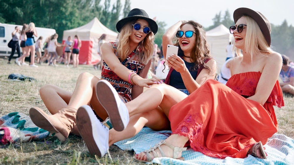 Junge Leute sitzen an einem Festival in der Wiese.