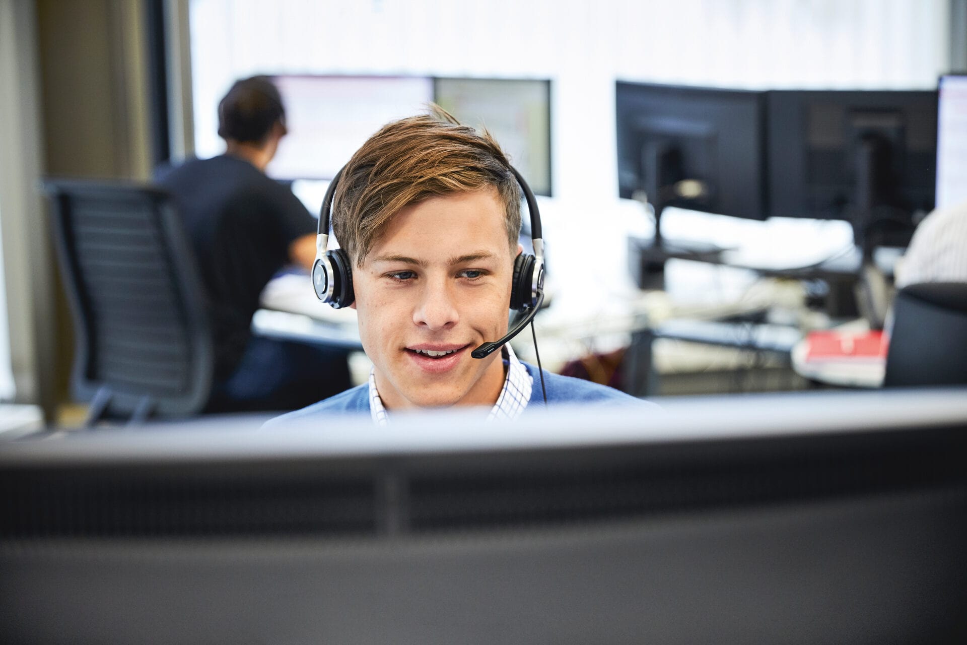 Mann sitzt mit Headset in einem Callcenter vor einem Bildschirm und telefoniert.