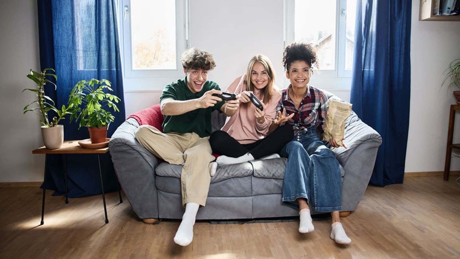 3 junge Menschen spielen auf dem Sofa Videospiele