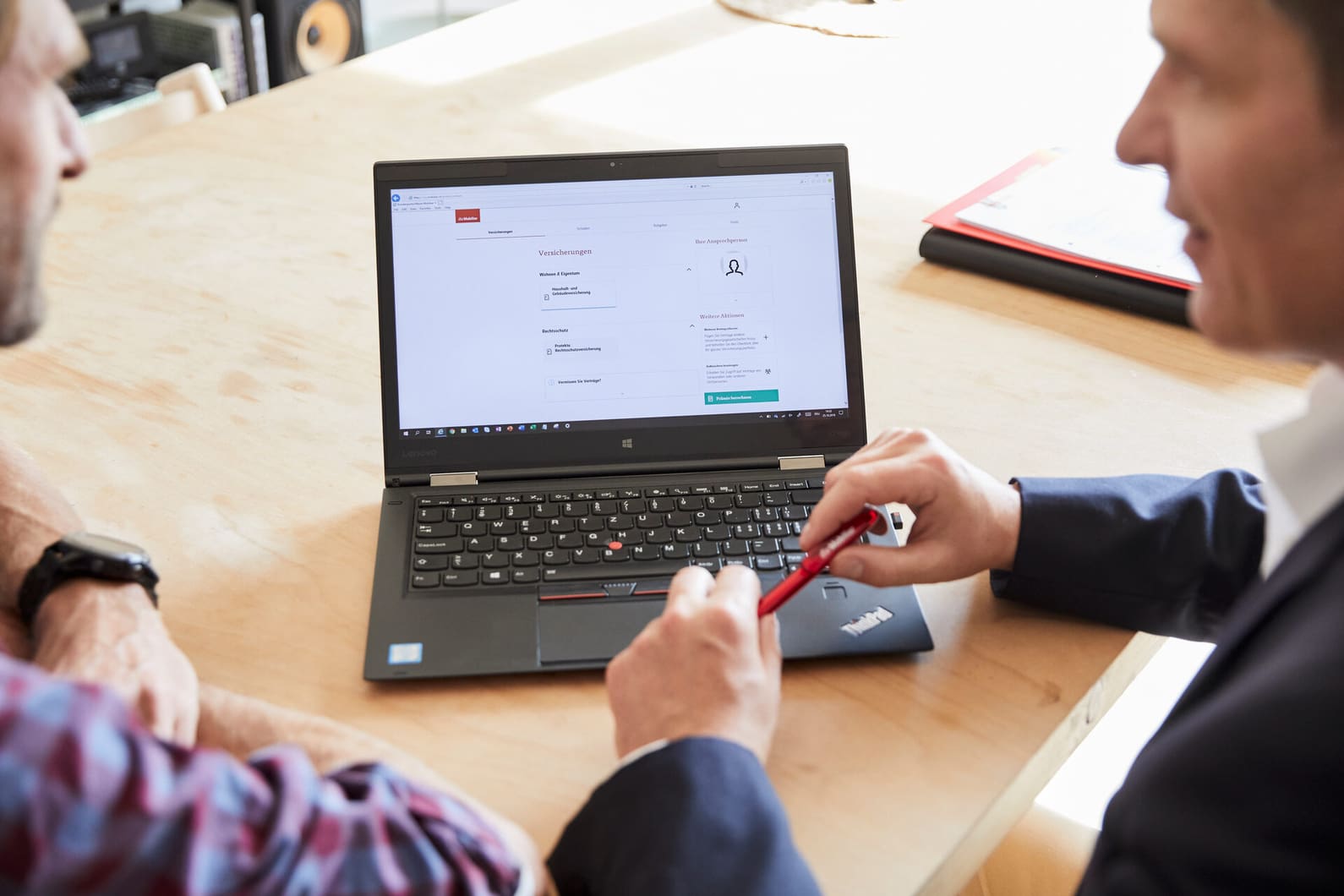Un conseiller en assurances de la Mobilière mène un entretien de conseil avec un client. Nous voyons un ordinateur portable sur une table et deux hommes regardant l’écran de derrière.