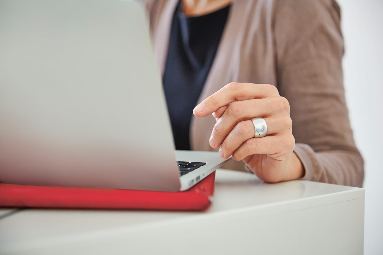 Eine Frau arbeitet am Laptop. Sichtbar sind nur ihre linke Hand und Oberkörper.