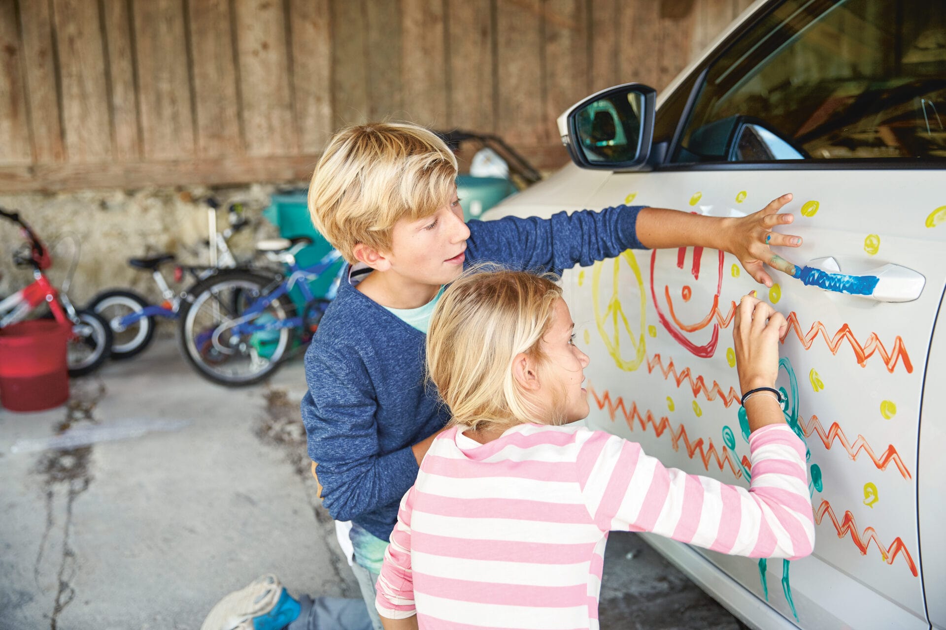 Due bambini dipingono l’auto con le dita.