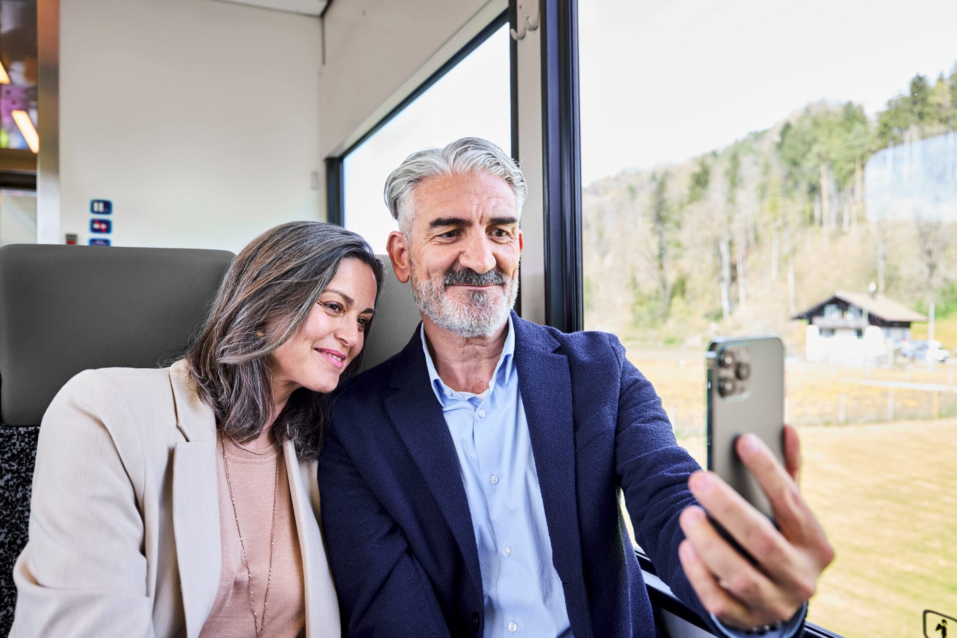 Eine Frau und ein Mann in Ihren Fünfzigern, sitzen zusammen im Zug und machen ein Selfie. 