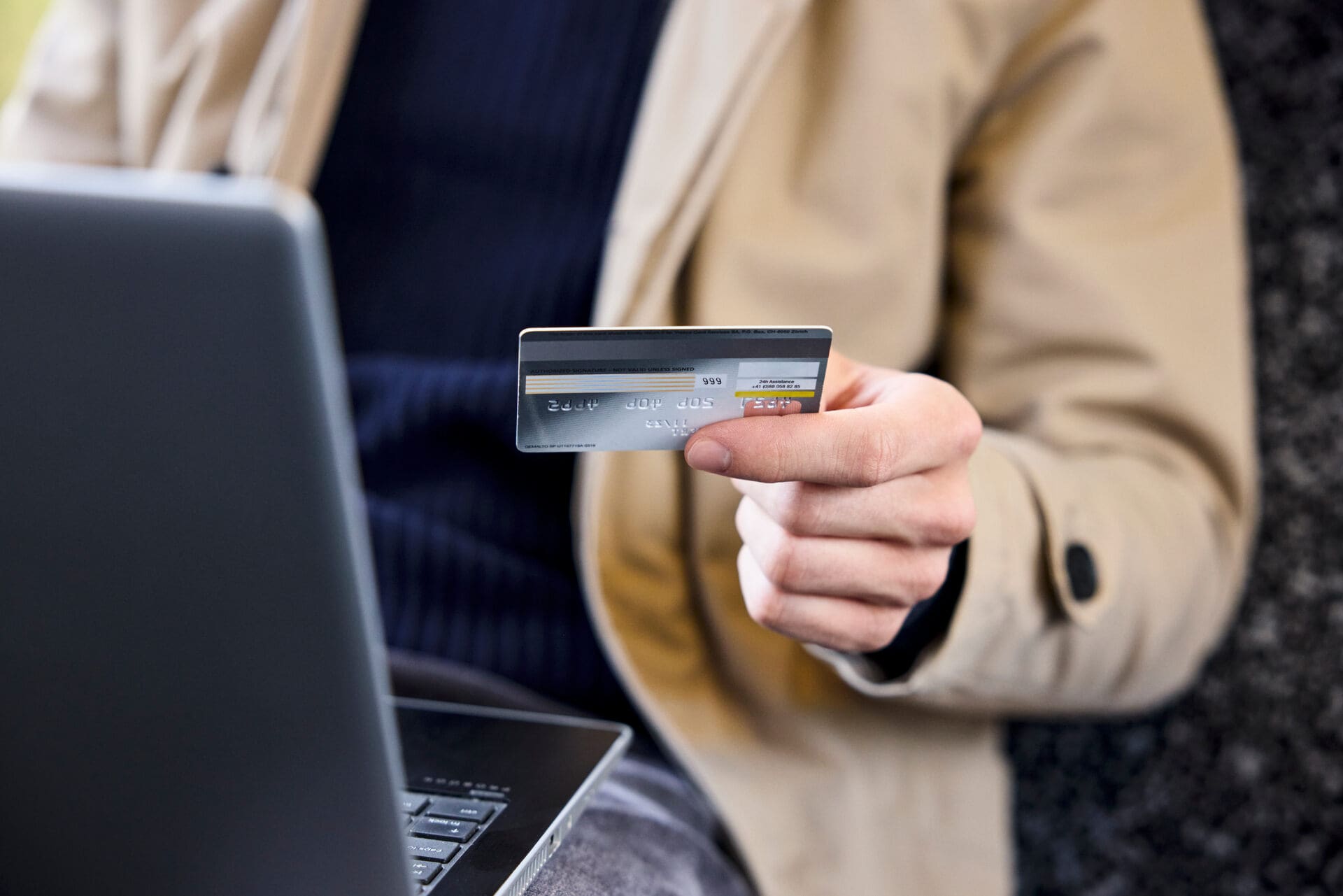 Mann mit Kreditkarte in der Hand und Laptop auf dem Schoss als Symbolbild für Kündigung der Kreditkarte