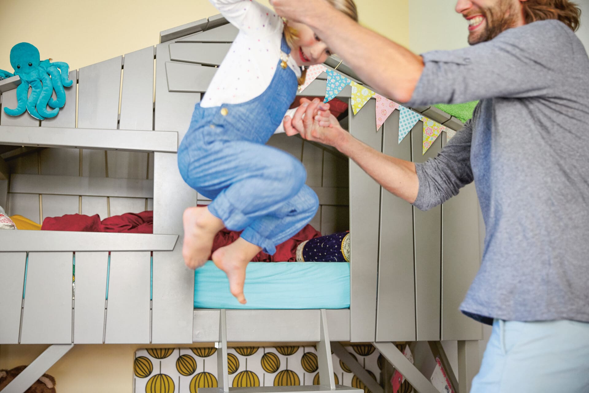 Un père joue avec sa fille, la tenant par les mains alors qu’elle saute en l’air. Tous deux rient et s’amusent.