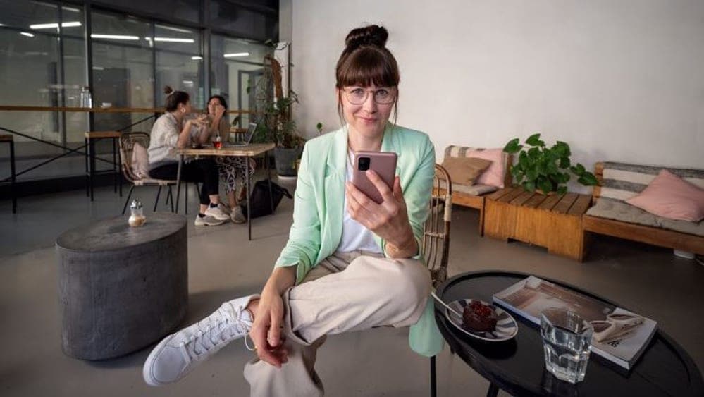 Eine junge Frau mit einem Handy in der Hand sitzt in einem Café.