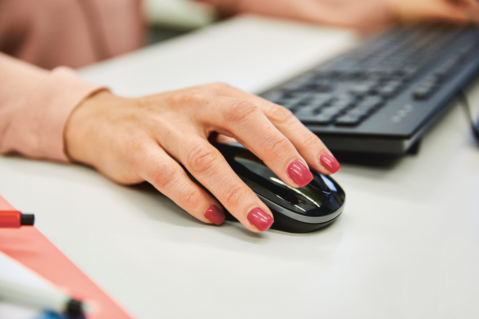Eine Hand mit lackierten Fingernägeln hält eine Computermaus, im Hintergrund ist eine Tastatur zu sehn. Symbolbild für Betreibung online einleiten.