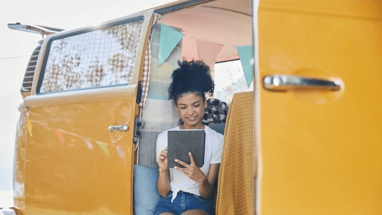 Eine Frau sitzt in einem gelben Minibus und schaut sich etwas am Tablet an.