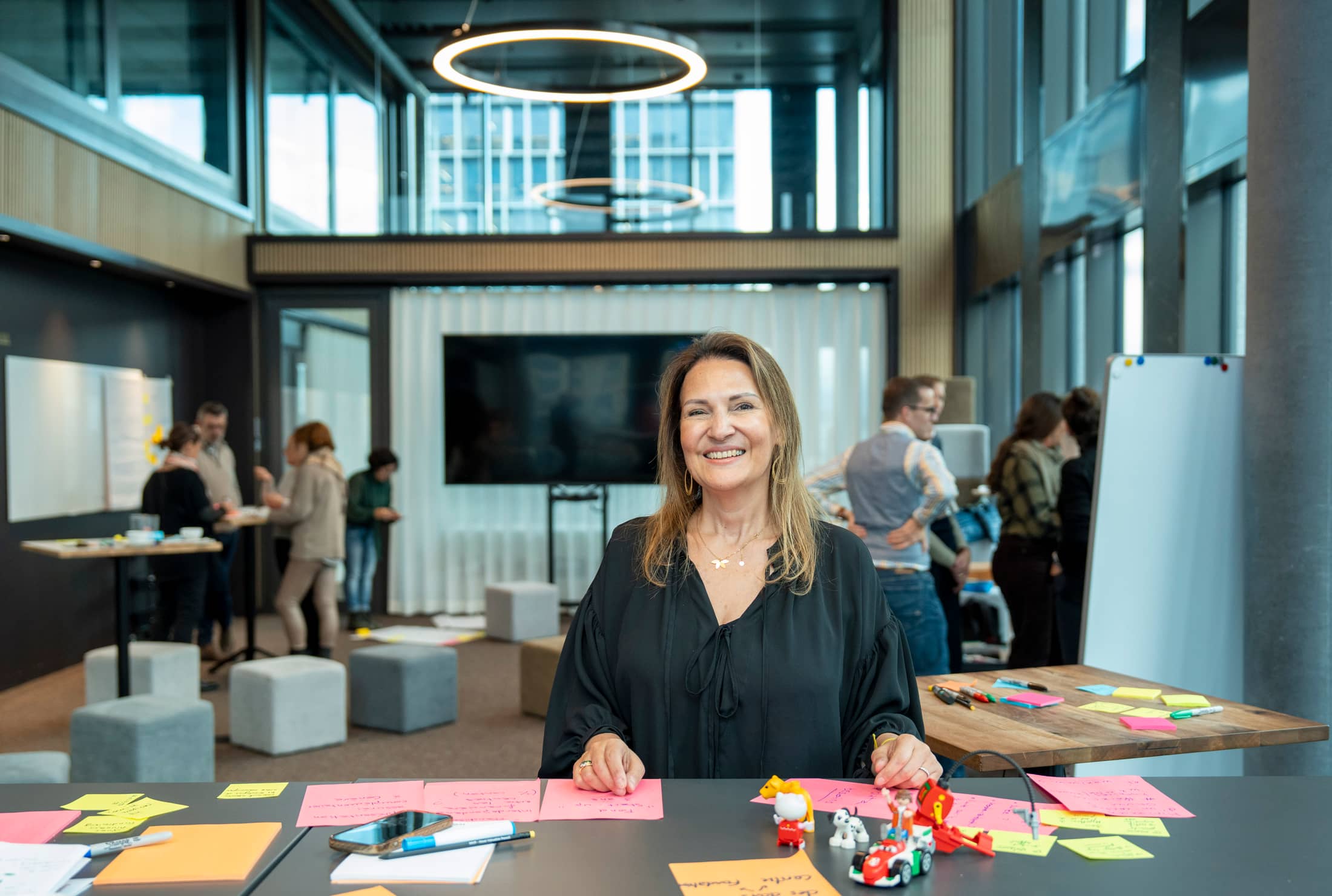Linda Kamal im Workshop des Mobiliar Forums, mit Post-its vor sich, blickt in die Kamera; Teilnehmende im Hintergrund unscharf.