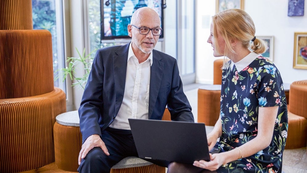 Ein Mann und eine Frau diskutieren etwas, die Frau hat einen Laptop in den Händen.