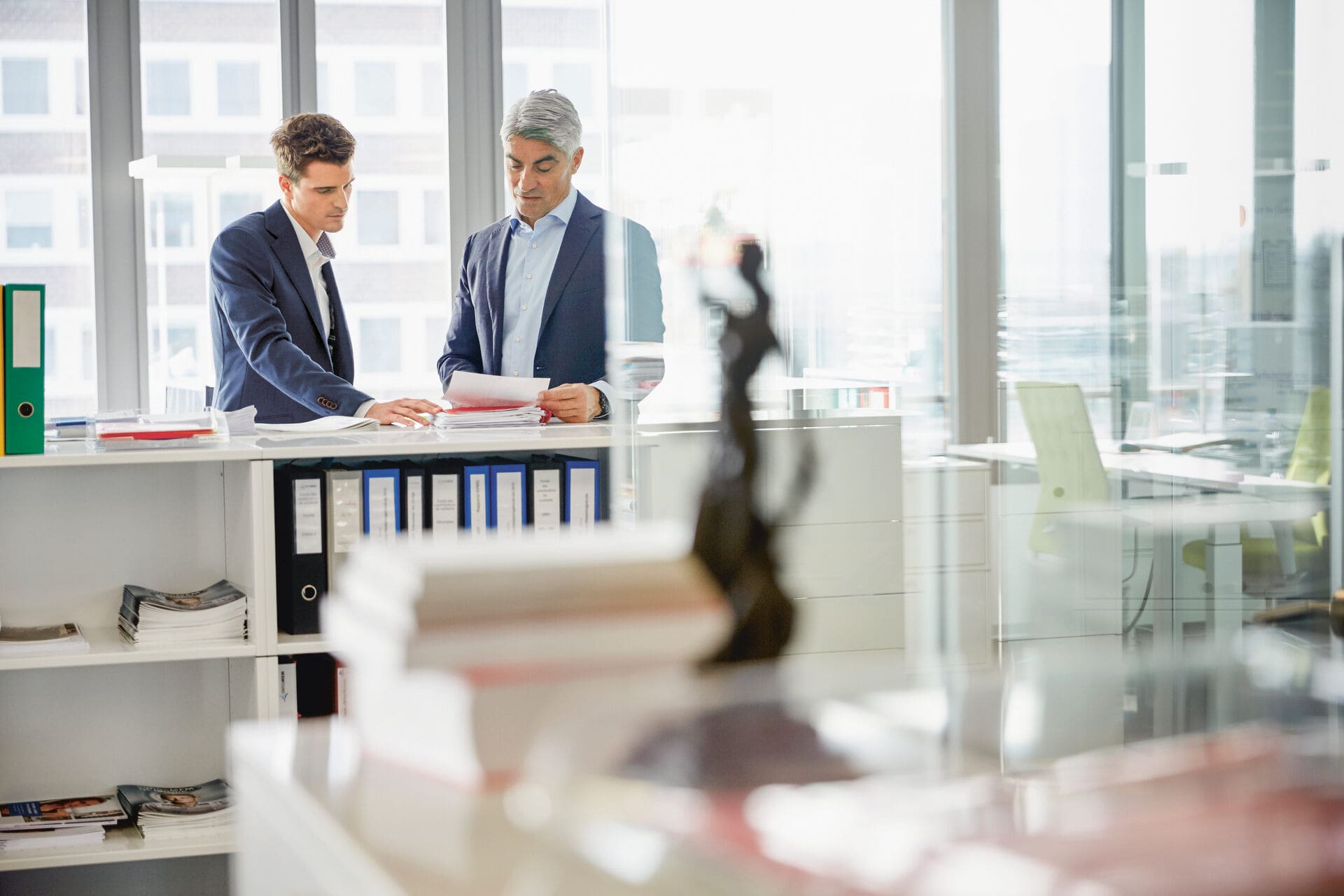 Eine Justizia-Skulptur steht auf einem Aktenschrank. Dahinter blicken zwei Männer in Anzügen auf ein Kündigungsschreiben und prüfen die Gründe einer fristlosen Kündigung.