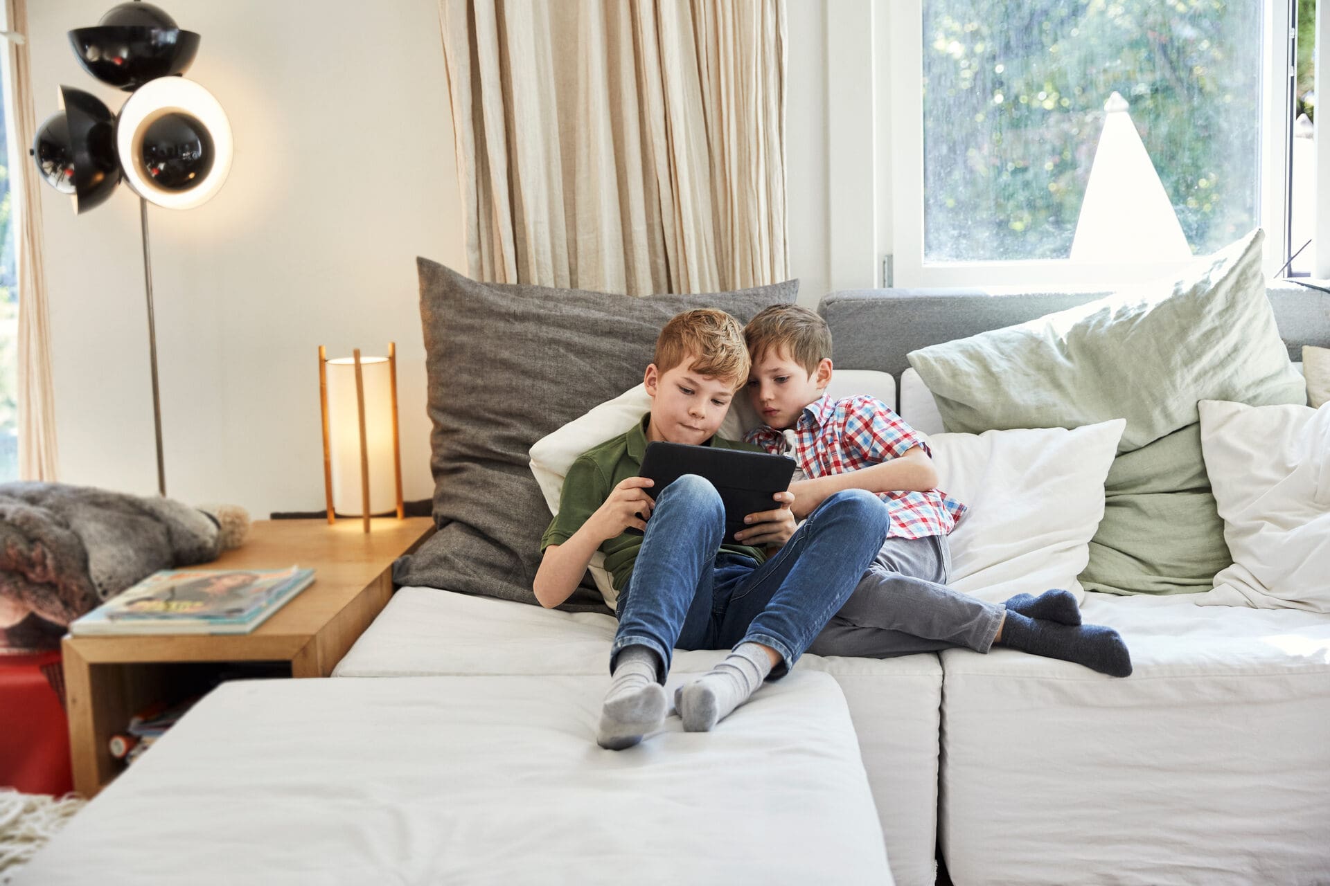 Deux enfants jouant avec une tablette sur le sofa familial 