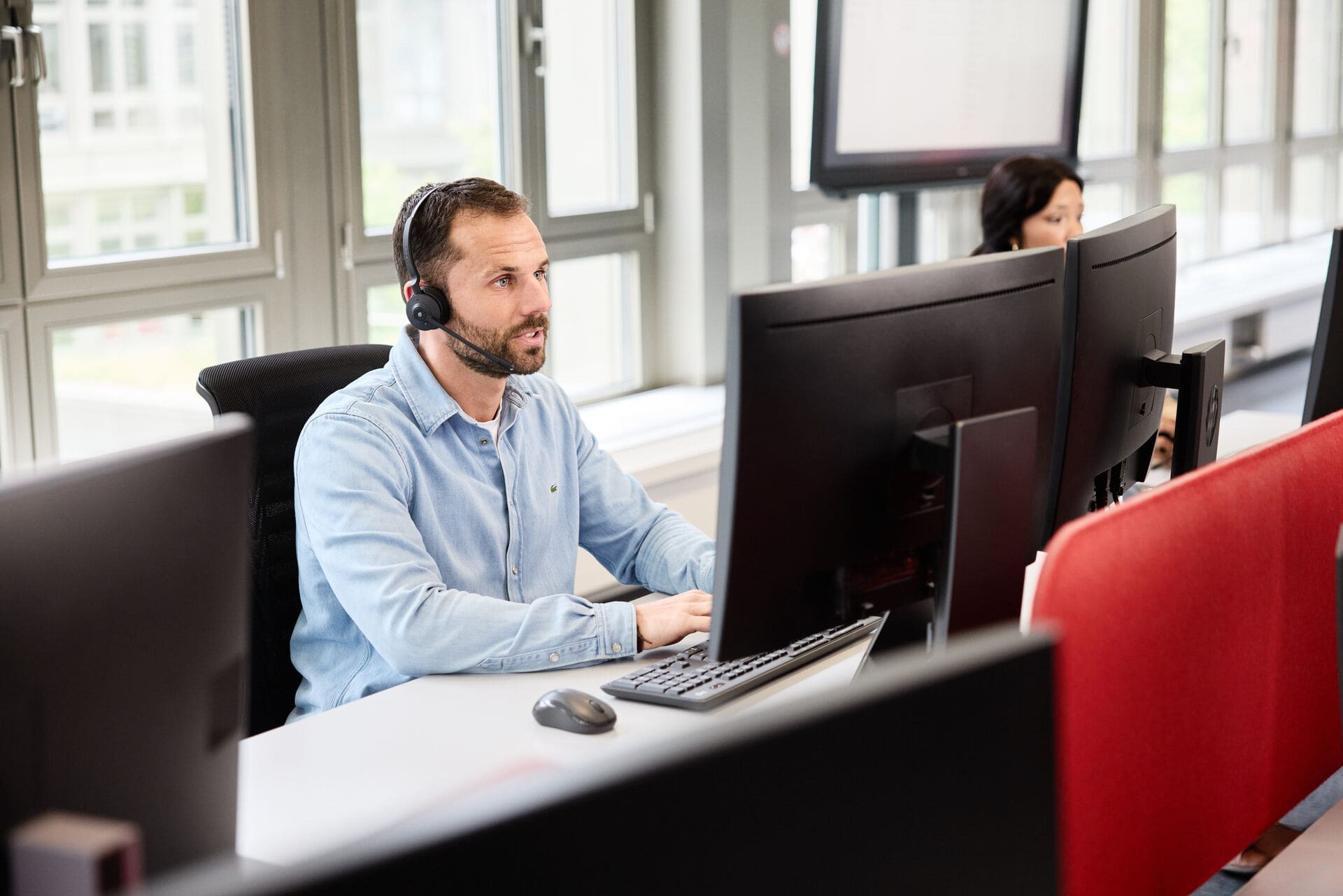 Mann sitzt mit Headset in einem Callcenter vor einem Bildschirm und telefoniert.