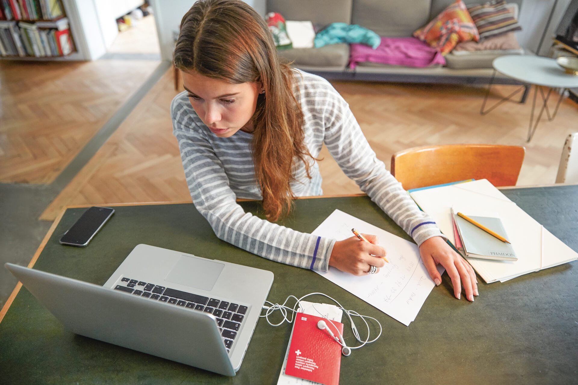 Une femme est assise à une table avec devant elle un laptop et son passeport; elle prend des notes sur son droit aux vacances.