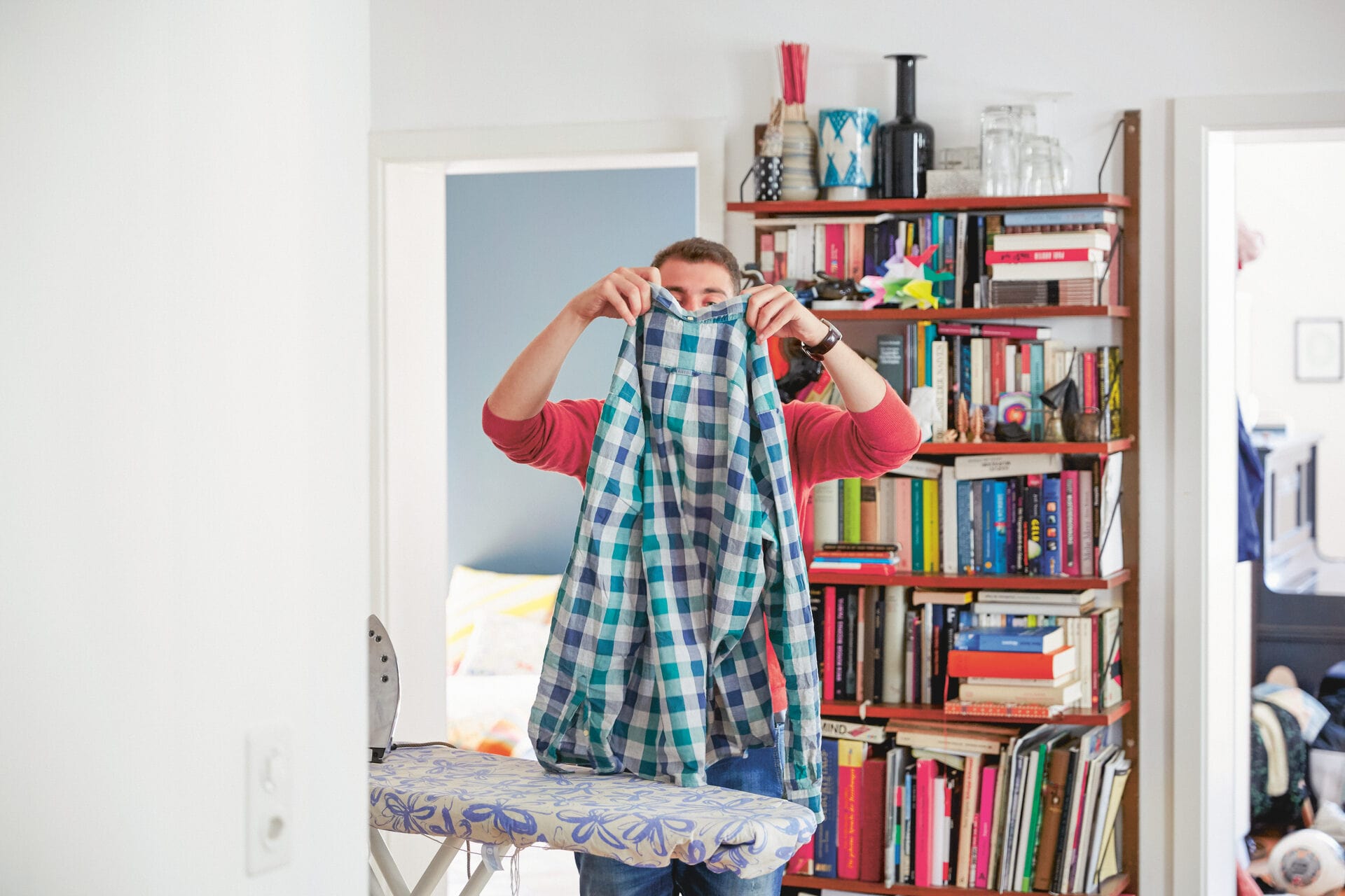 Mann hebt ein kariertes Hemd hoch und sortiert die Wäsche als Symbolbild für die Zuordnung der Nebenkosten.