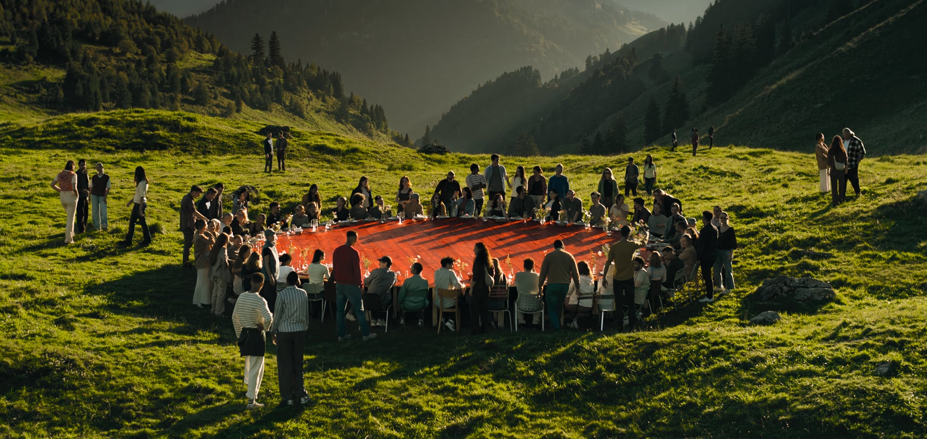 Une grande table rouge dans la nature autour de laquelle de nombreuses personnes sont assis.