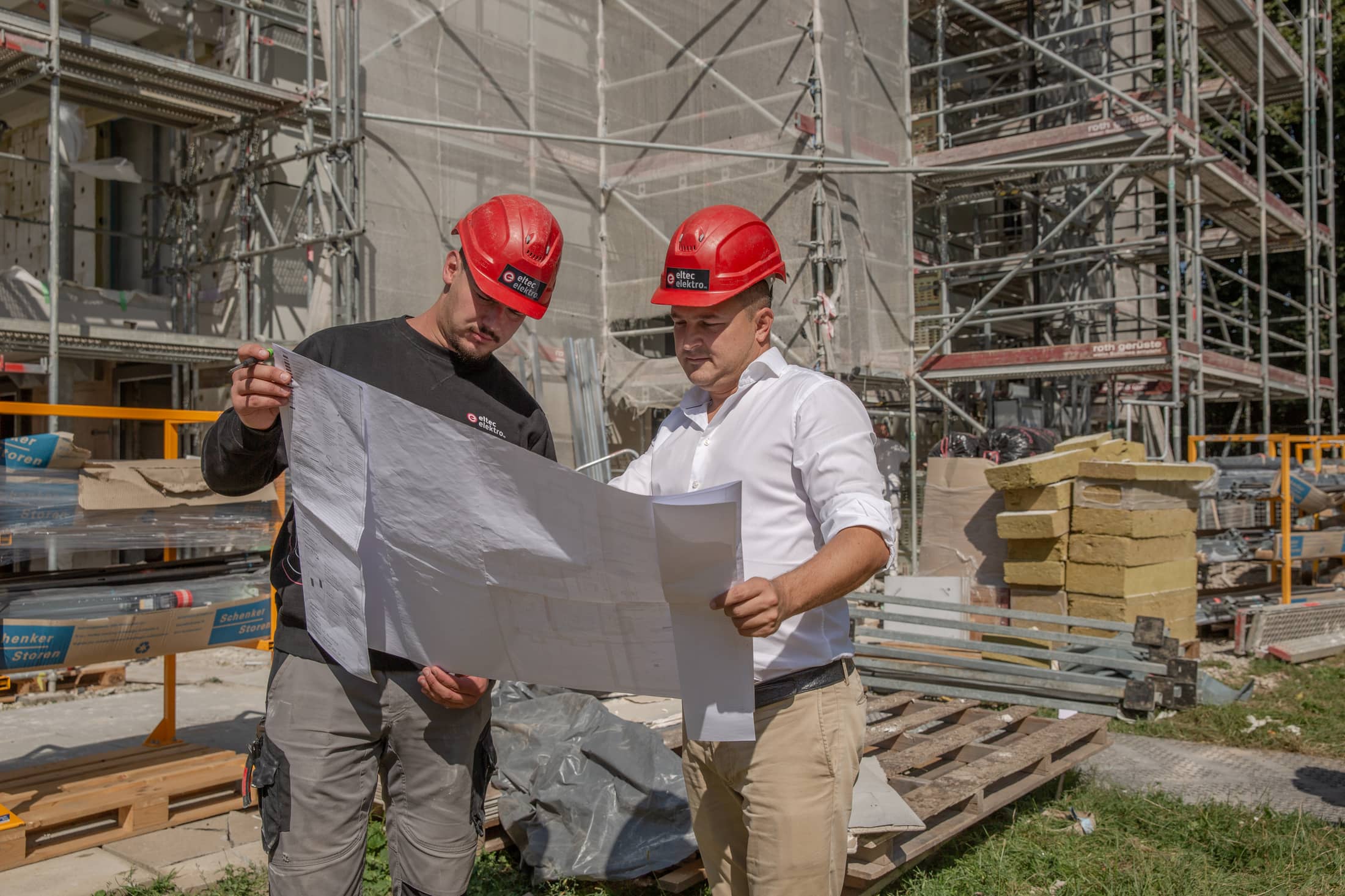 Tomislav Soldo, Inhaber des Geschäfts Eltec Elektro, steht mit einem Mitarbeiter auf einer Baustelle. Sie blicken gemeinsam auf Baupläne.